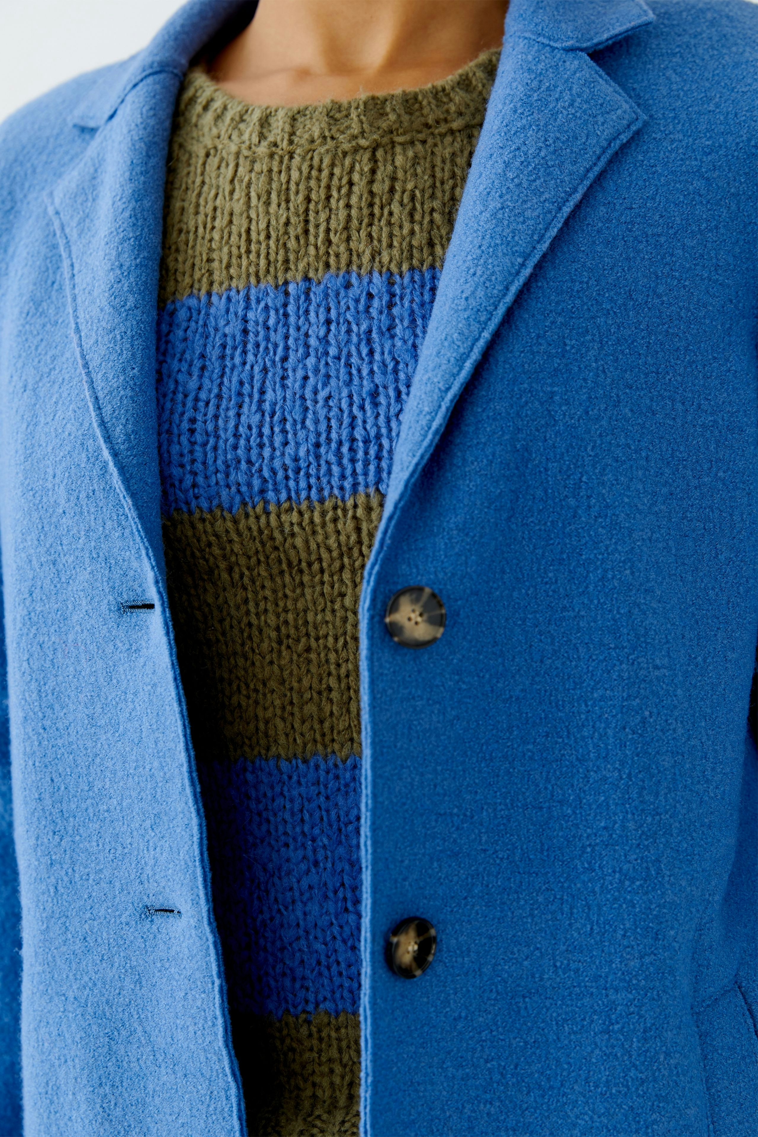 Wool coat: A woman in a blue wool coat over a green striped pullover, showcasing a casual style.