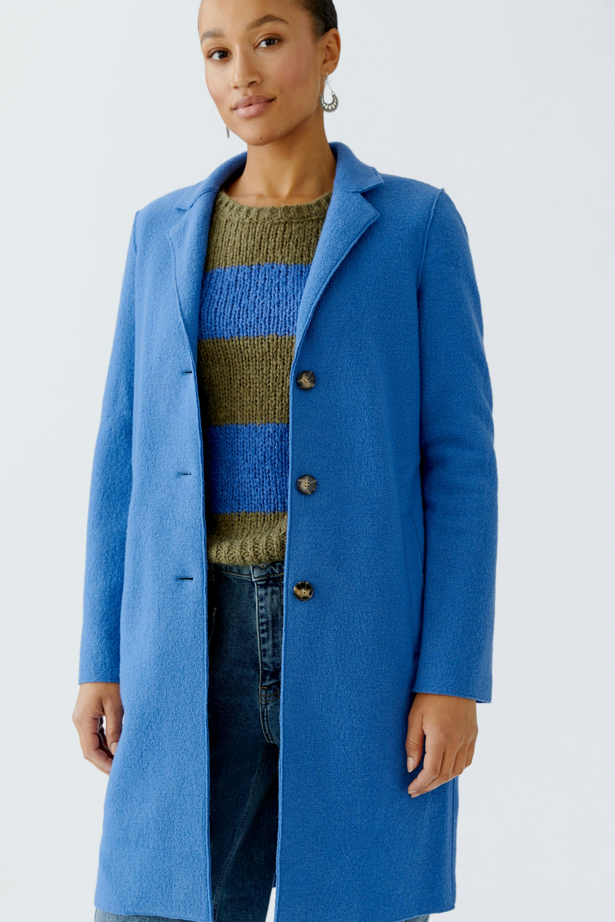 Modern women's wool coat: Woman in a blue coat over a striped pullover, paired with jeans.