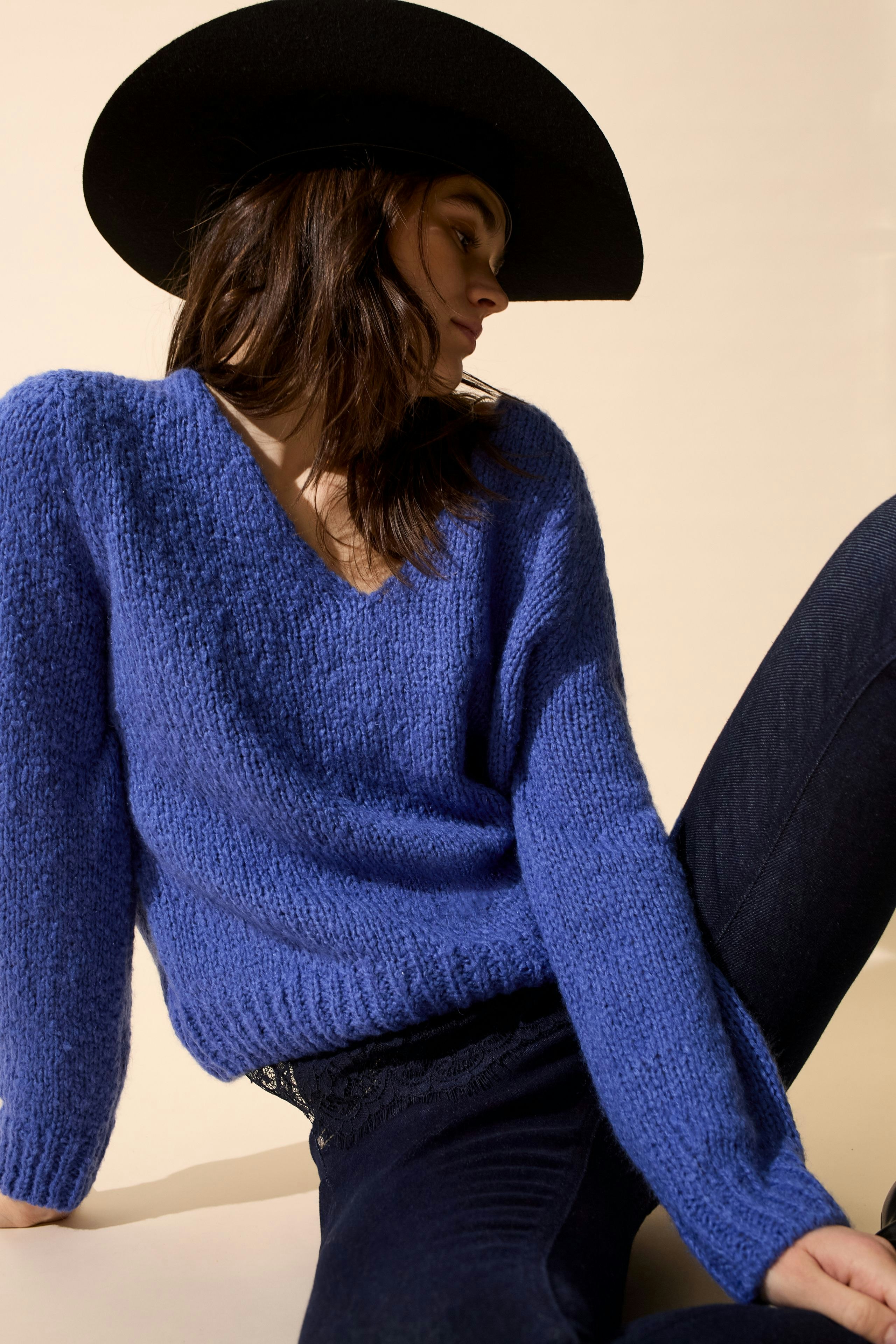 Skinny jeans: Woman in blue pullover and black hat poses casually.
