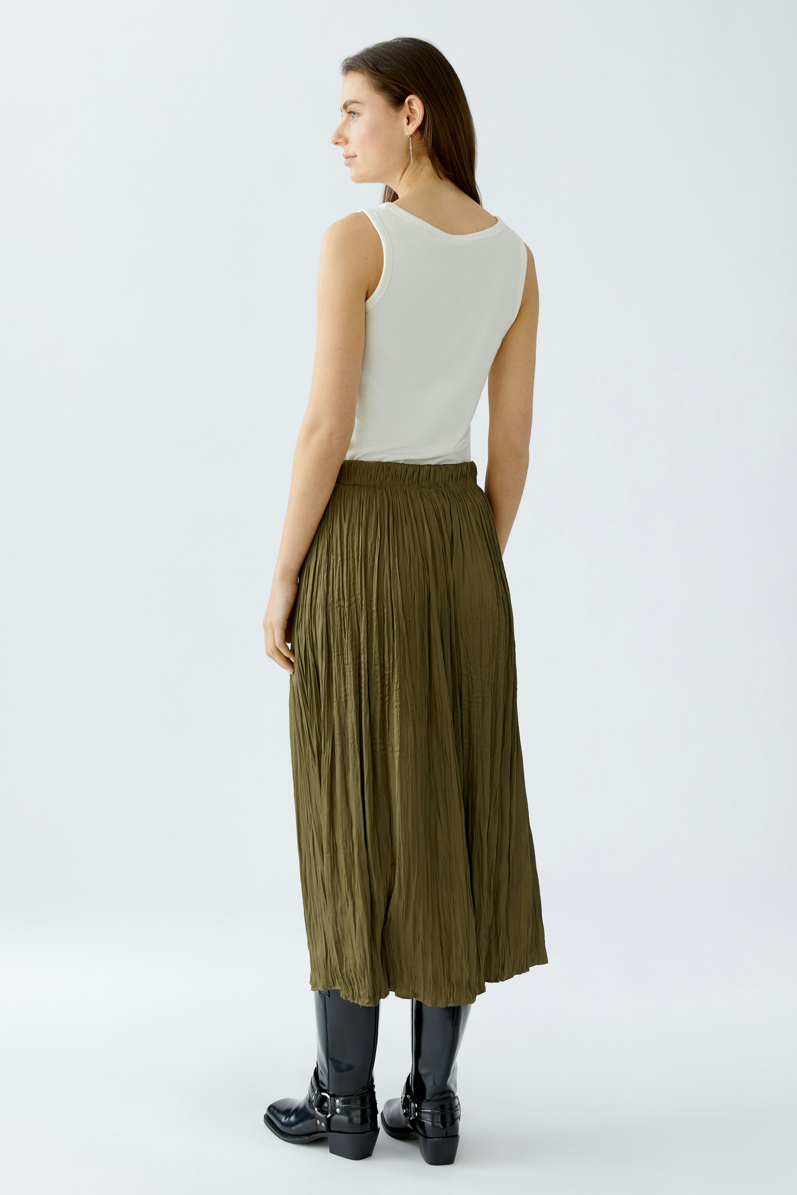 Damen Maxirock: Frau in einem plissierten, olivgrünen Maxirock mit lässigem Top und Stiefeln.