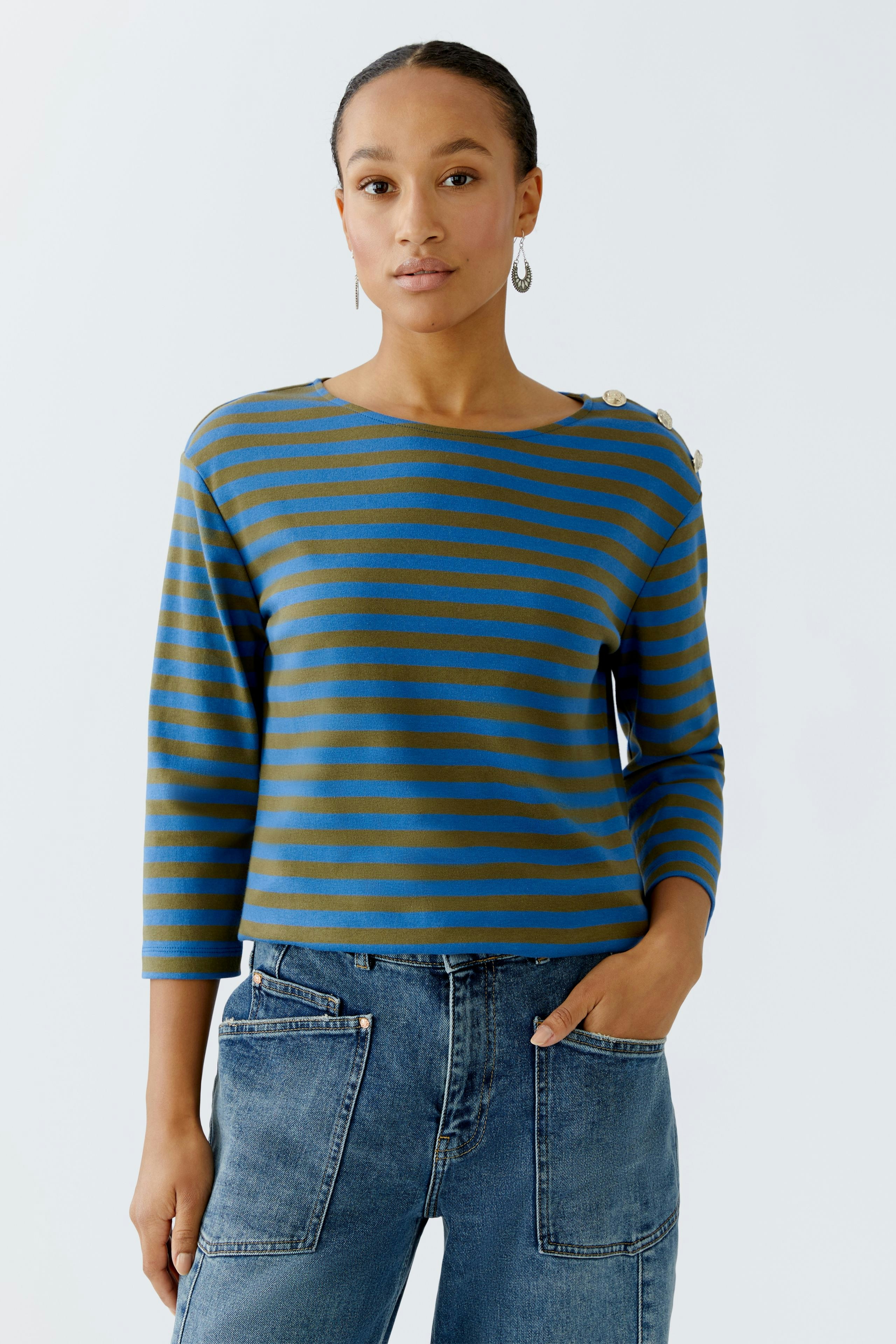 Damen Langarmshirt: Frau in gestreiftem Shirt mit Knöpfen an der Schulter und lässigen Jeans.