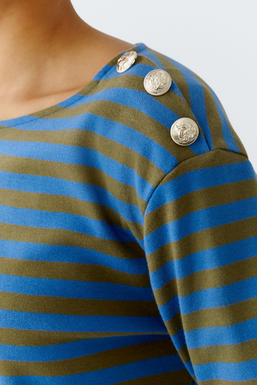 Casual long-sleeve shirt: Woman in a striped pullover with blue and green stripes and decorative buttons.