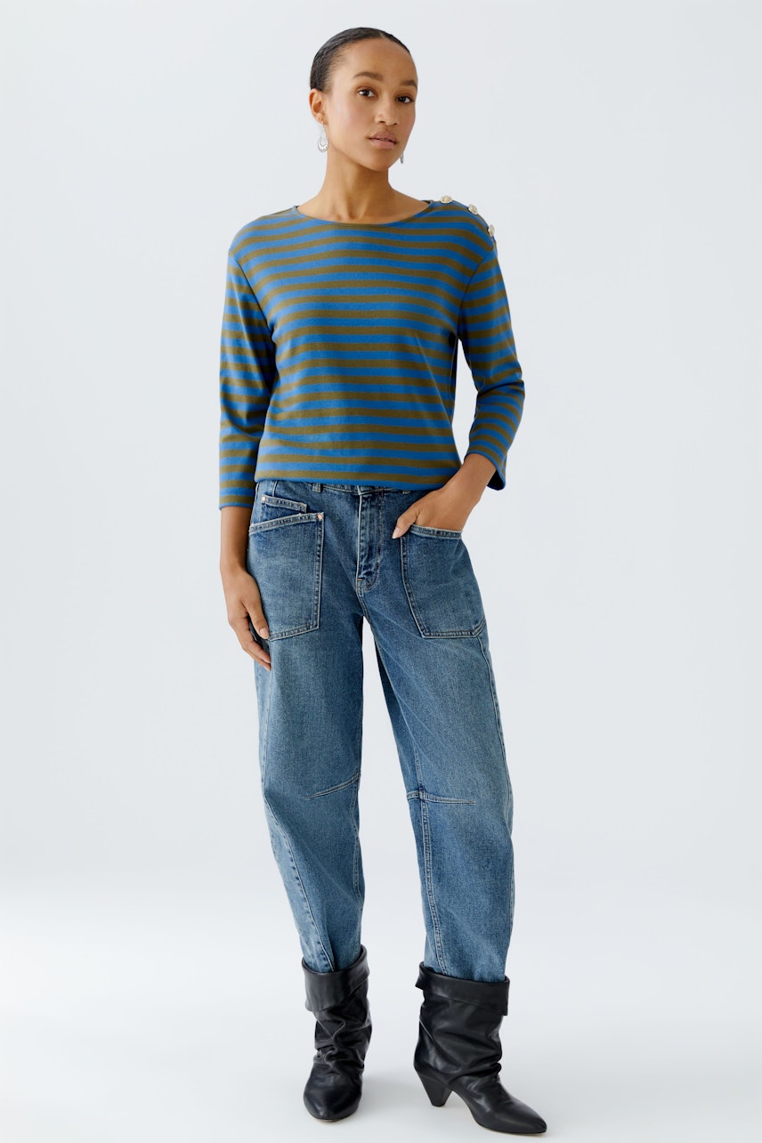 Casual women's long-sleeve shirt: Woman in a striped pullover with blue and green tones, paired with relaxed jeans.