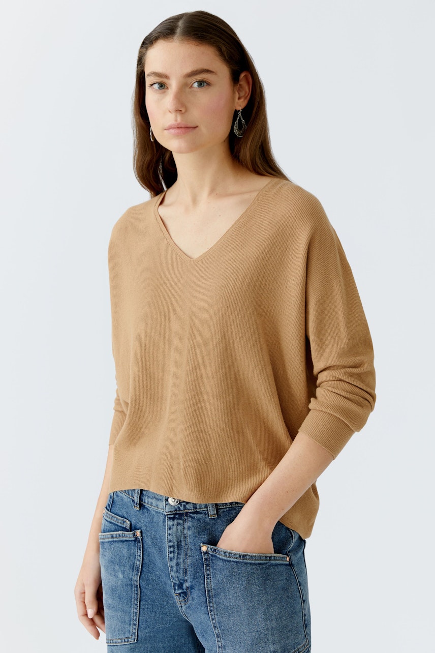Casual women's pullover: A woman in a beige V-neck pullover paired with blue jeans, looking relaxed.
