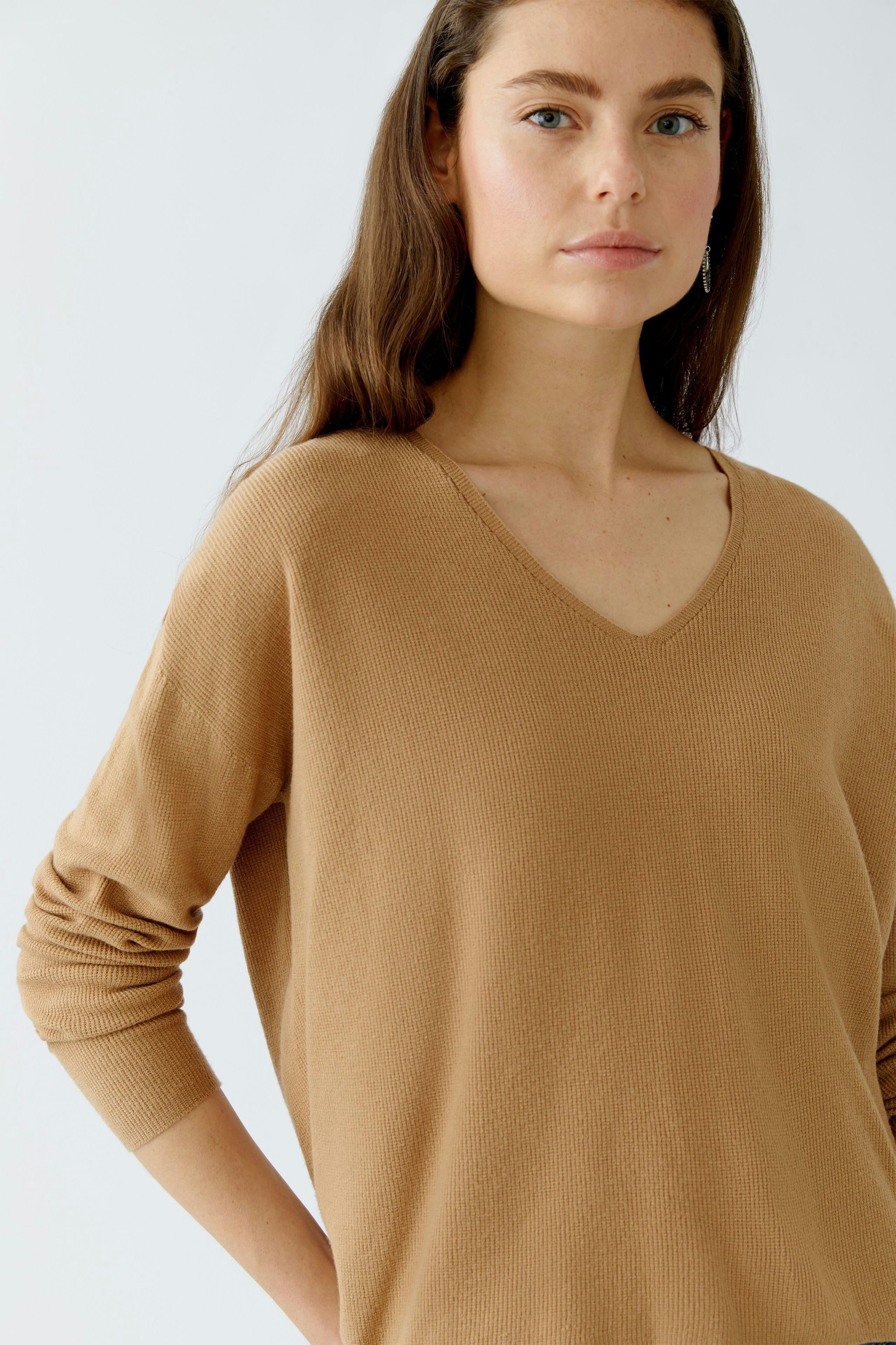 Beiger Damen-Pullover mit V-Ausschnitt, lässig und bequem, getragen von einer Frau mit natürlichem Look.