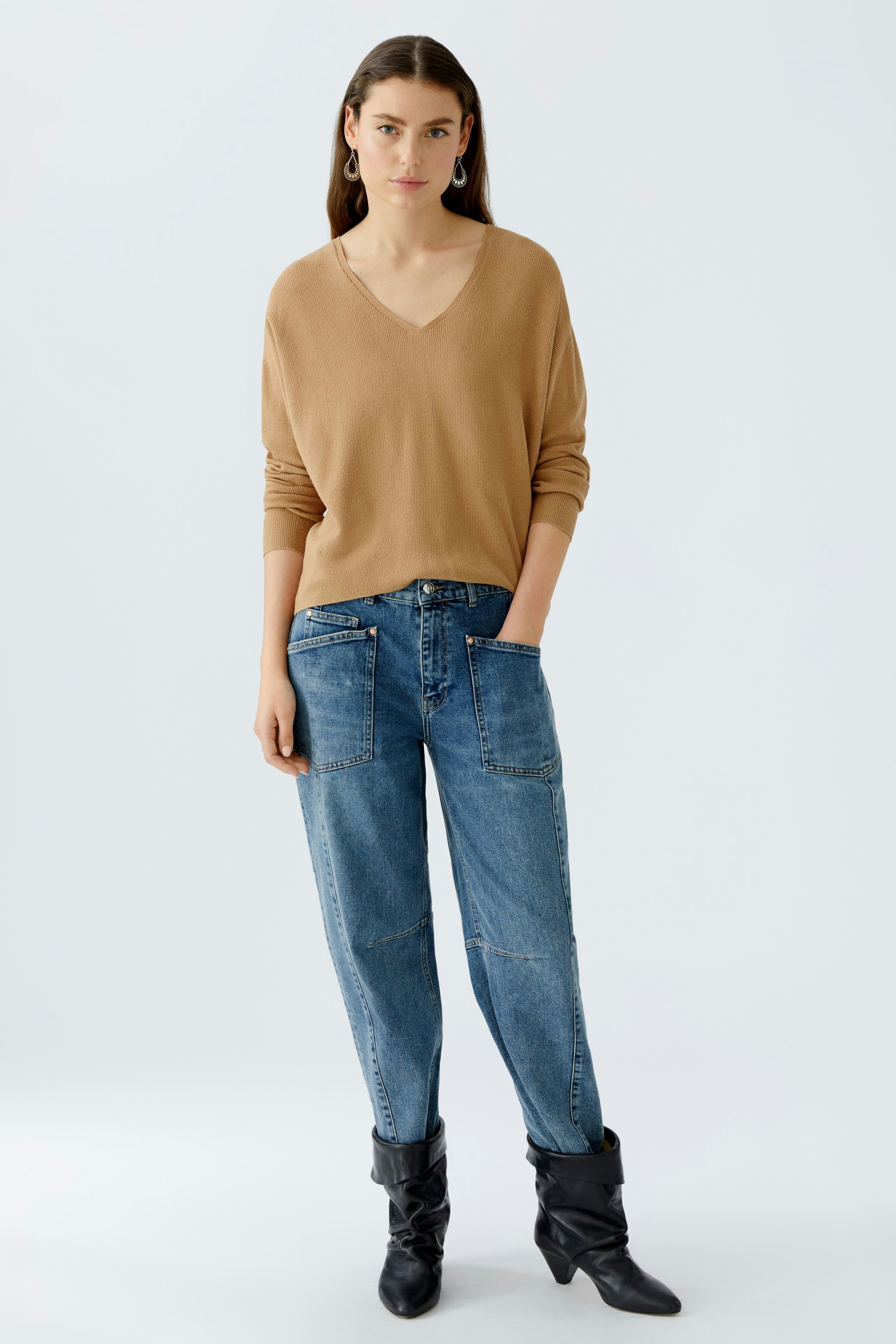 Beiger Damen-Pullover mit V-Ausschnitt, lässig kombiniert mit Jeans und Stiefeln.