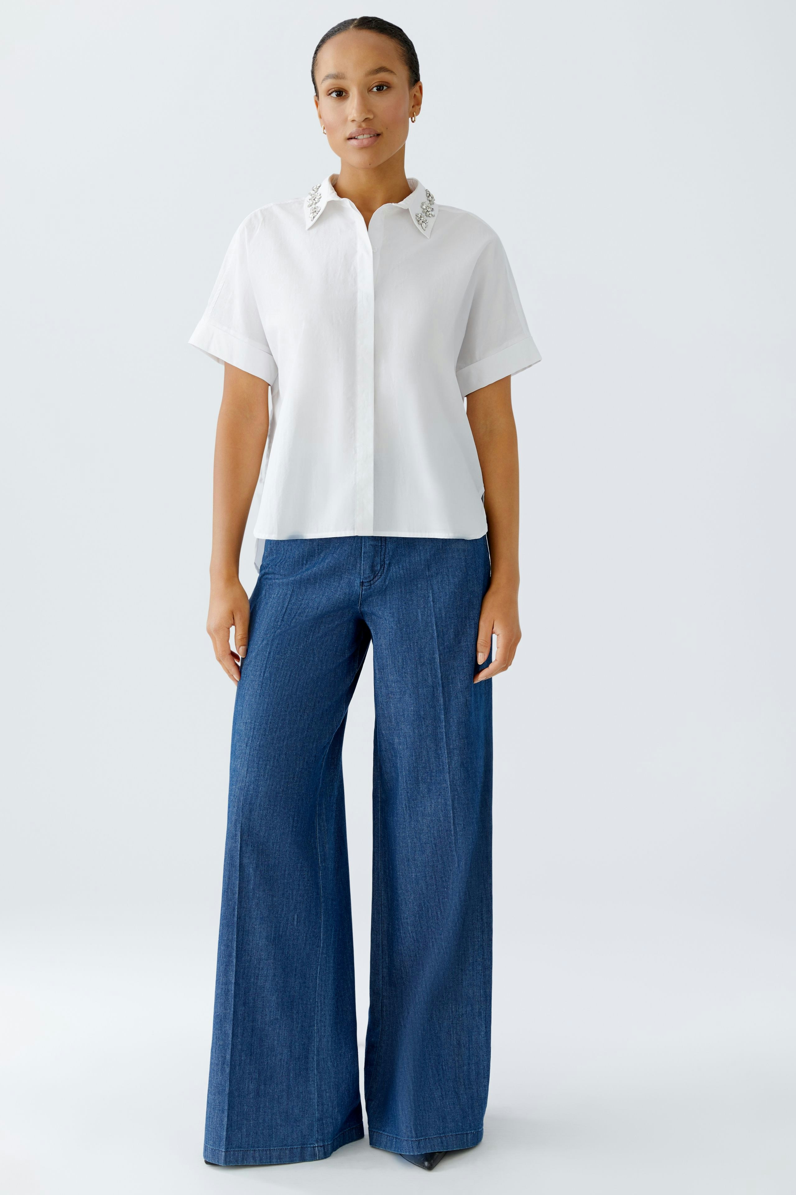Moderne Damen-Bluse: Frau in weißer Bluse mit dekorativem Kragen und lässigen Jeans.