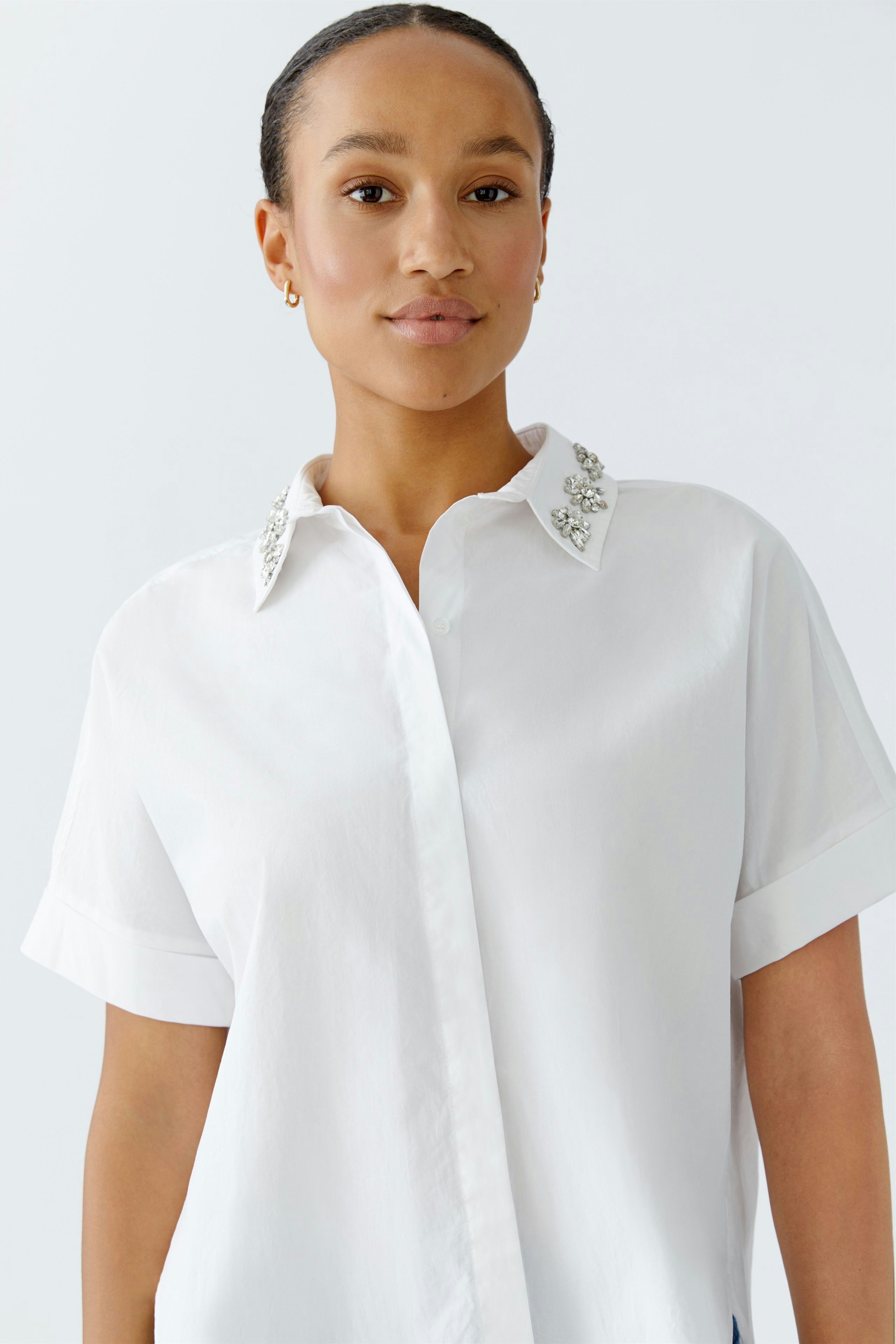 Moderne Damen-Bluse: Frau in weißer Bluse mit funkelnden Kragenakzenten, lässig und stilvoll.
