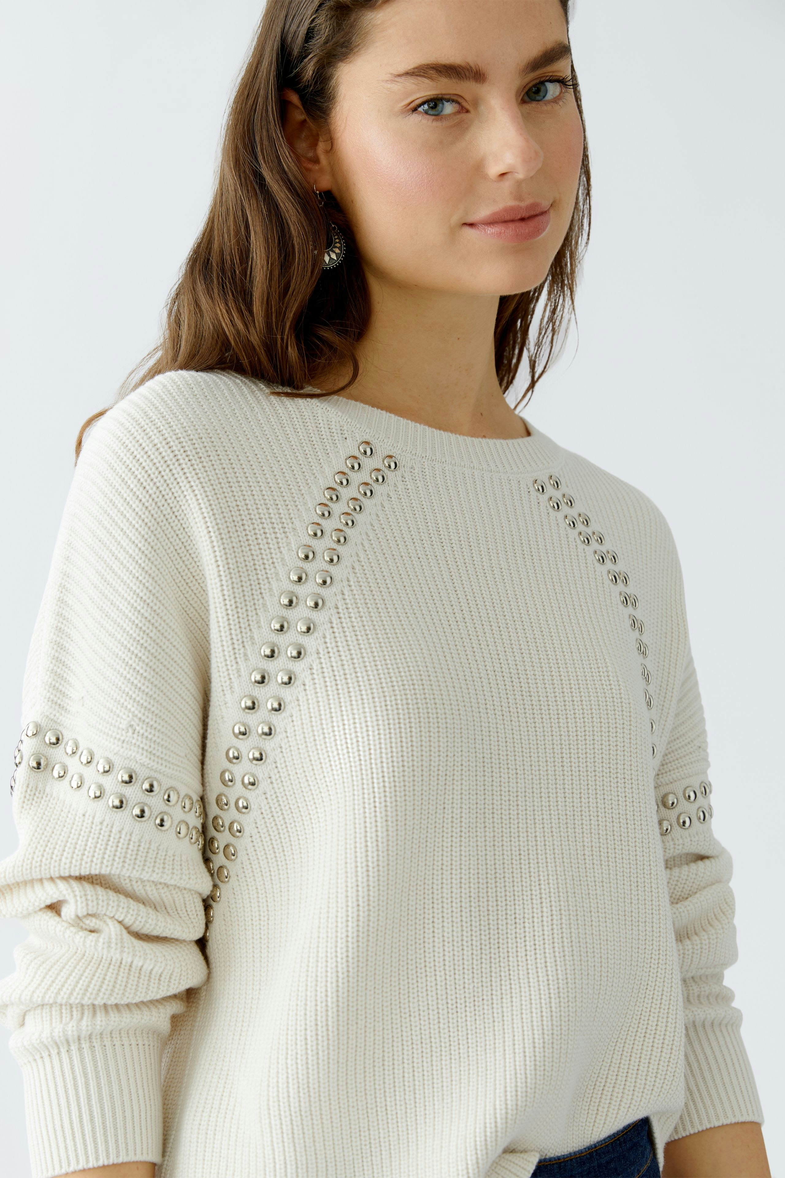Casual women's pullover: Young woman in a cream pullover with decorative studs, looking relaxed.