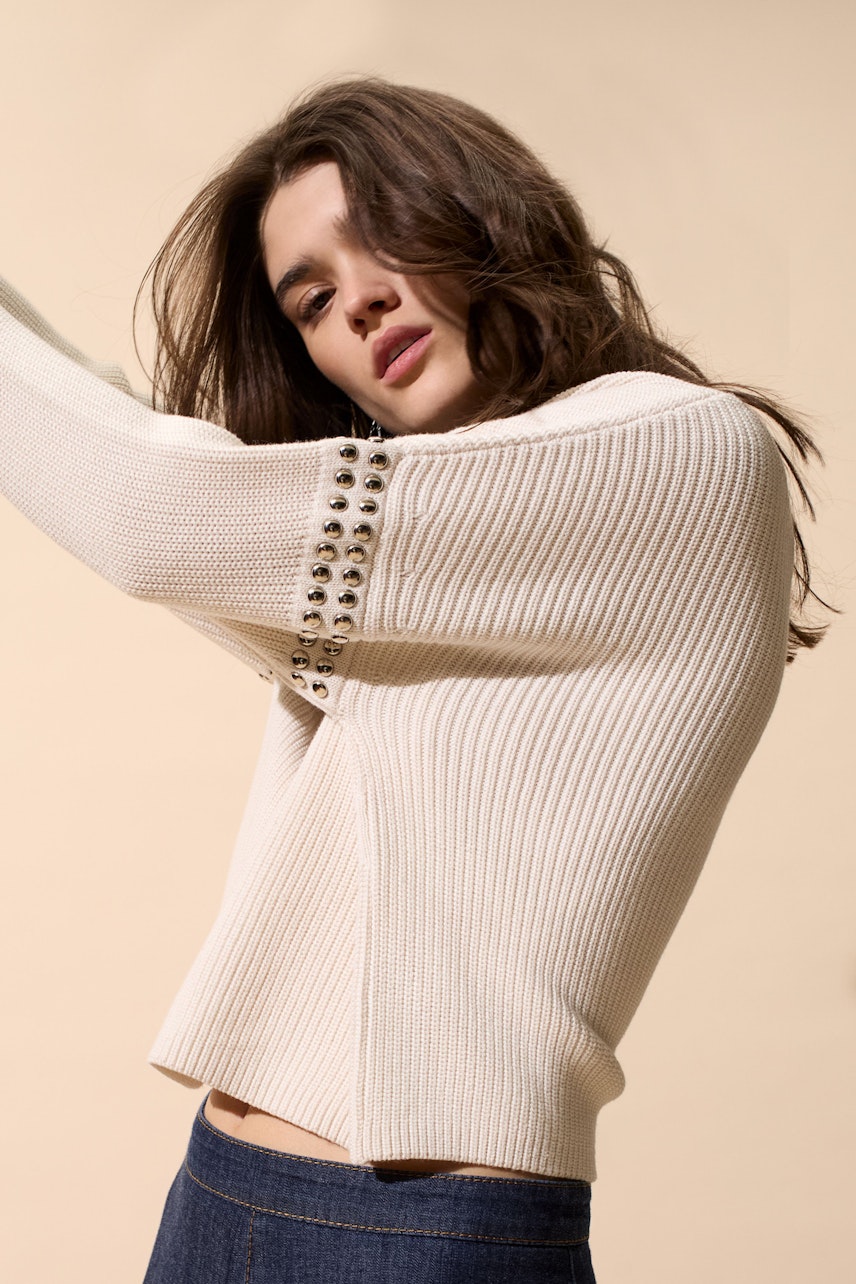 Modern women's pullover: A woman in a cream ribbed pullover with studded details poses confidently.