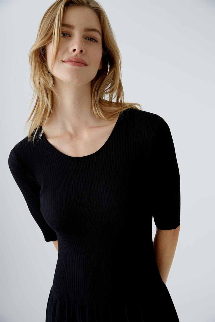 Schwarzes Strickkleid: Frau mit kurzen Ärmeln und weitem Rock, lässig und modern.