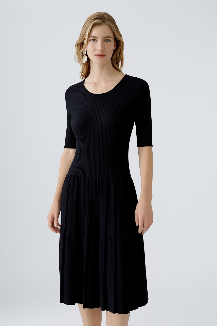 Schwarzes Strickkleid: Frau in einem taillierten, kurzärmligen Kleid mit weitem Rock.