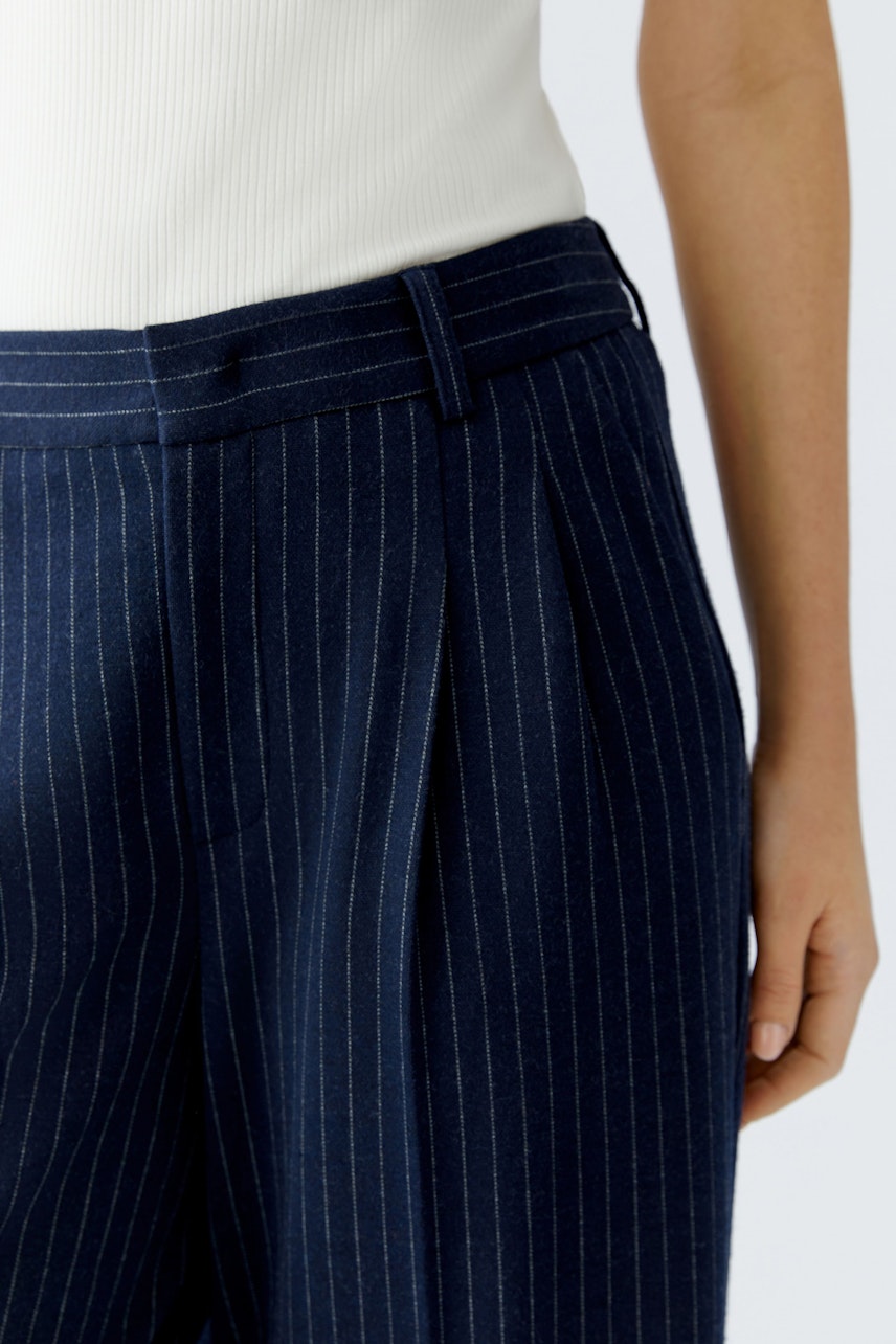 Bundfaltenhose: Dunkelblaue Hose mit feinen Streifen, lässig kombiniert mit einem weißen Oberteil.
