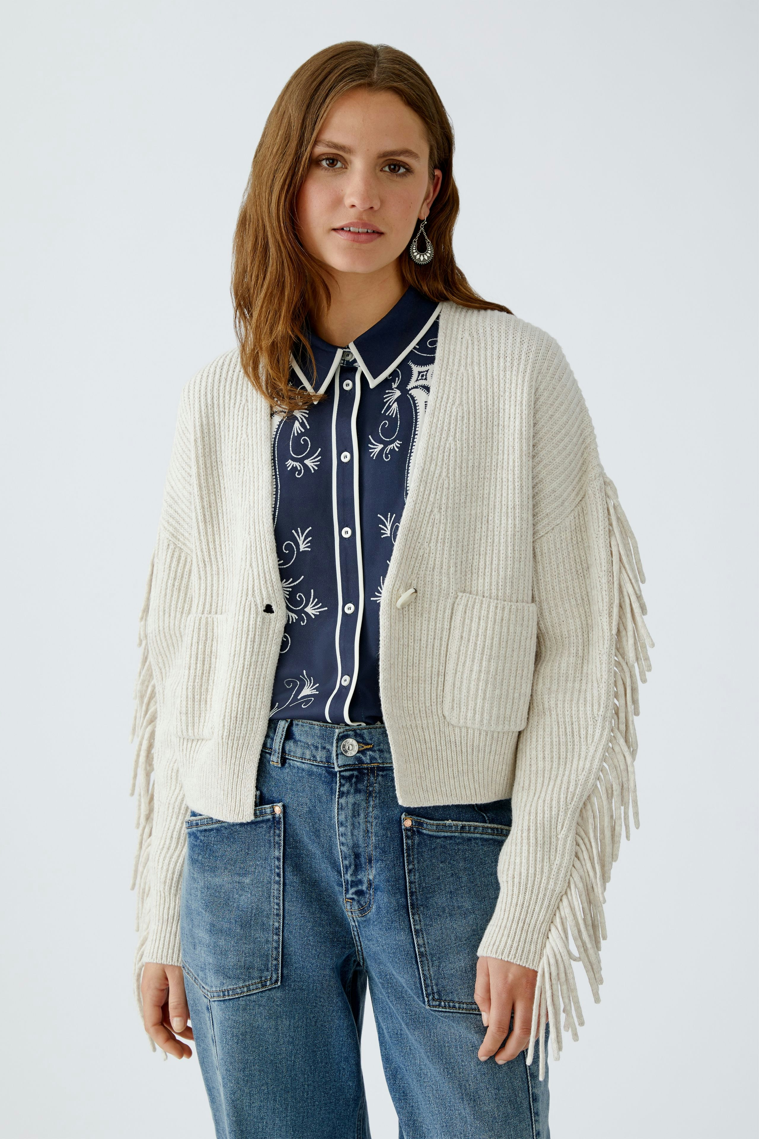 Casual women's cardigan: Young woman in a light beige cardigan with fringes and pockets, paired with a navy shirt.