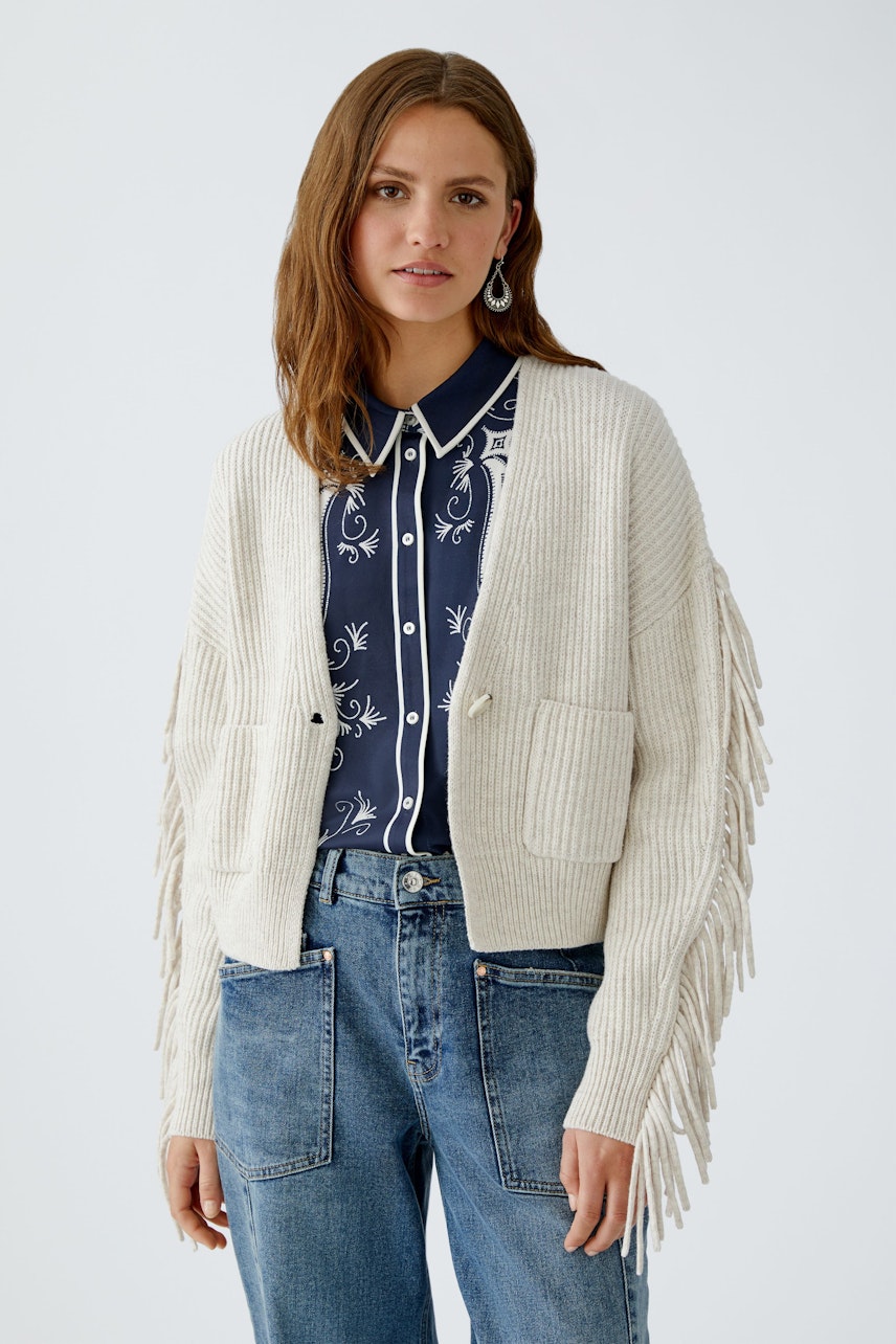 Casual women's cardigan: Young woman in a light beige cardigan with fringes and pockets, paired with a navy shirt.