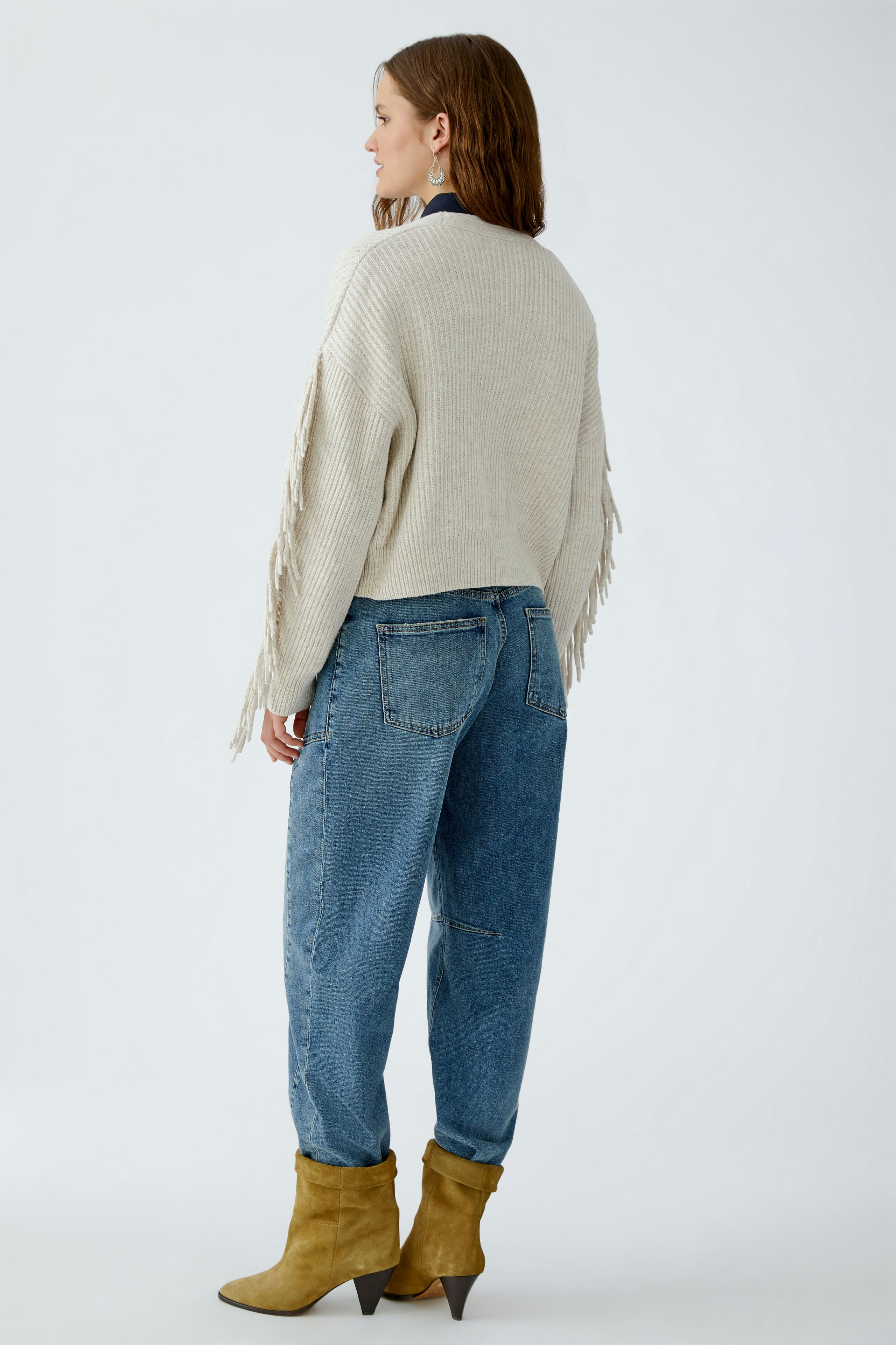 Casual women's cardigan: A woman in a light beige cardigan with fringes, paired with blue jeans.