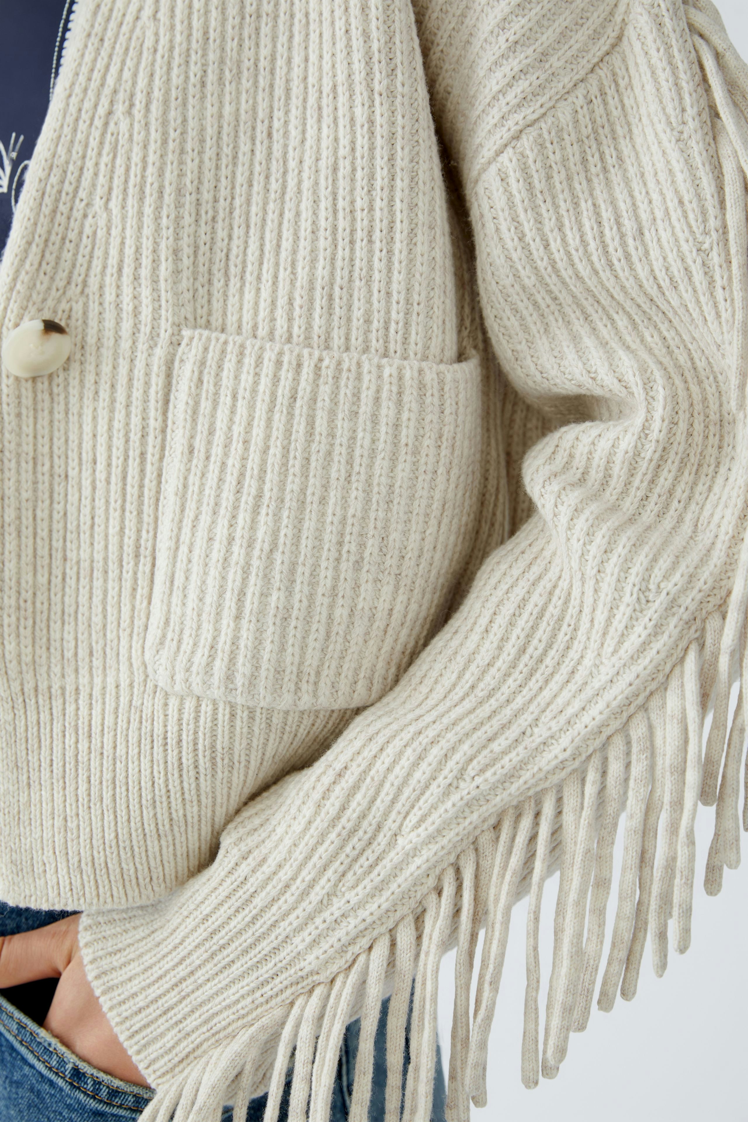 Casual women's cardigan: Close-up of a woman in a beige ribbed cardigan with fringe details.