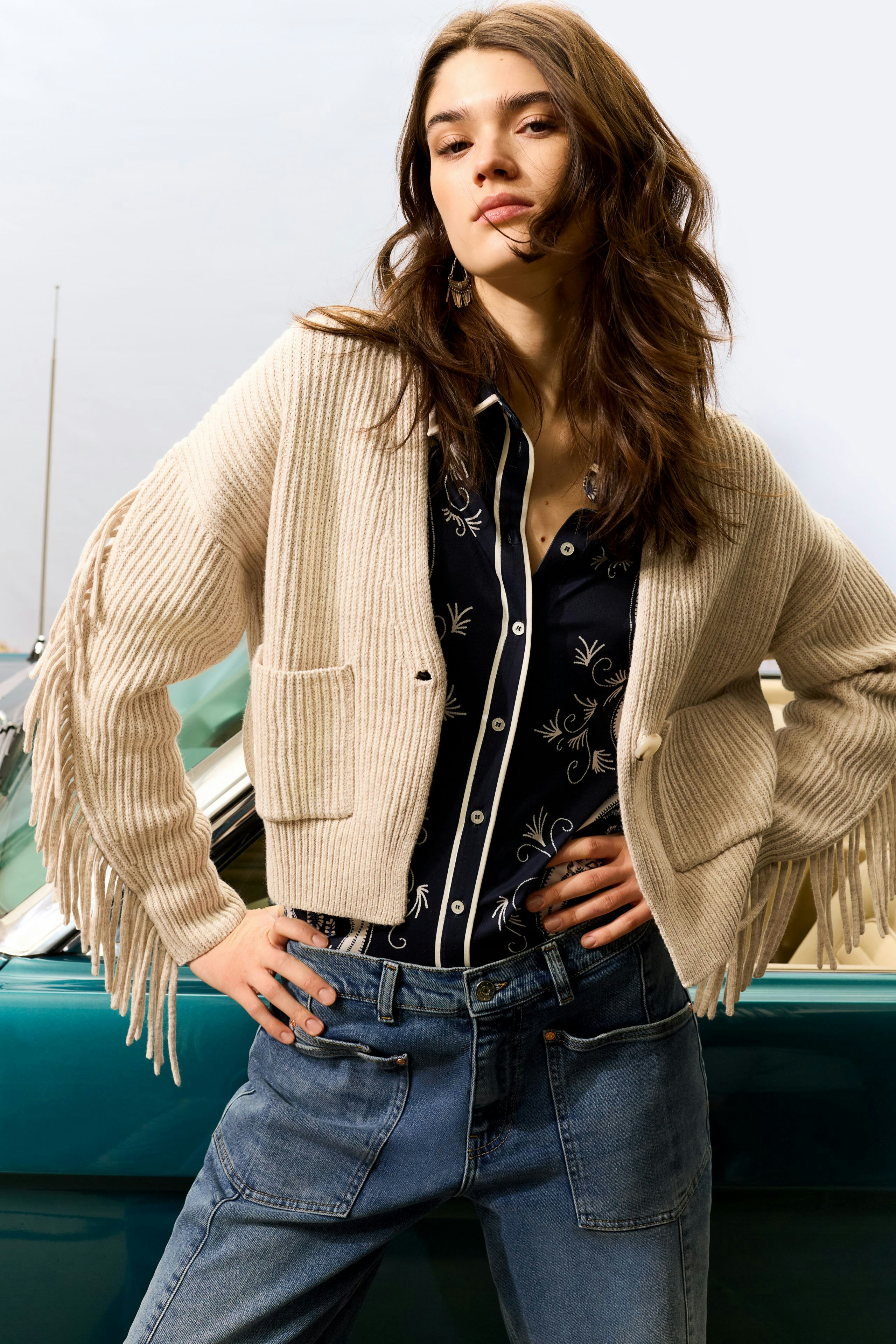 Casual women's cardigan: A woman in a beige cardigan with fringe details, paired with a patterned shirt.