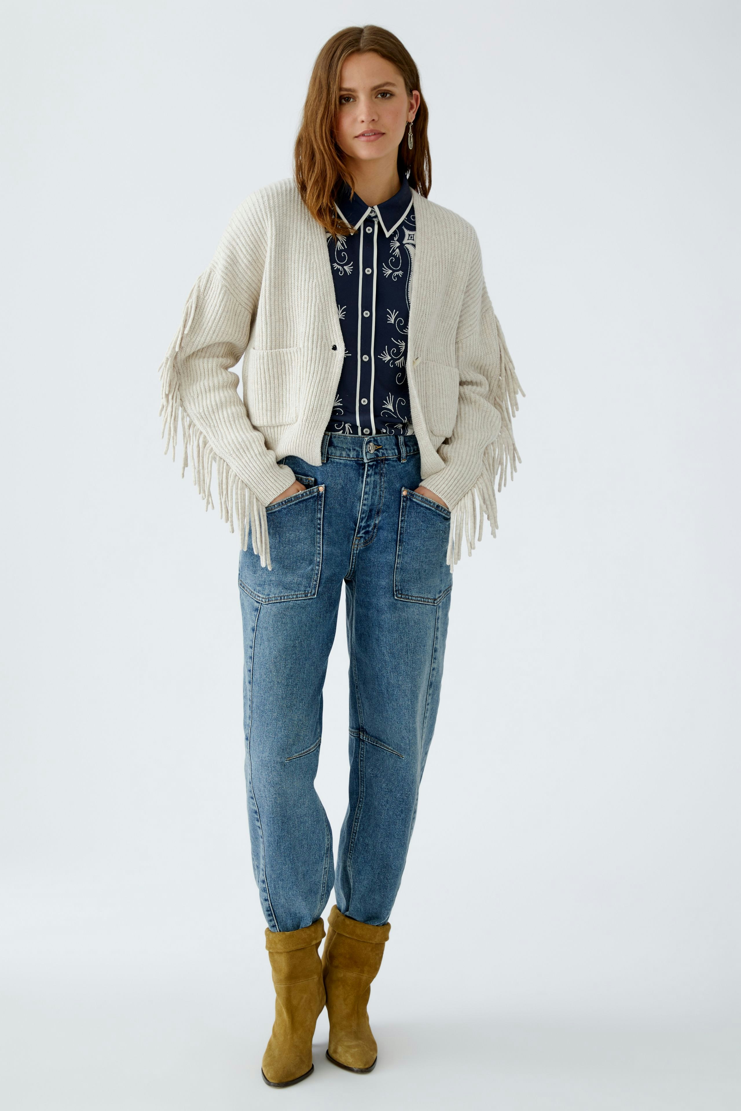 Casual women's cardigan: A woman in a cream cardigan with fringe details, paired with a patterned shirt and jeans.
