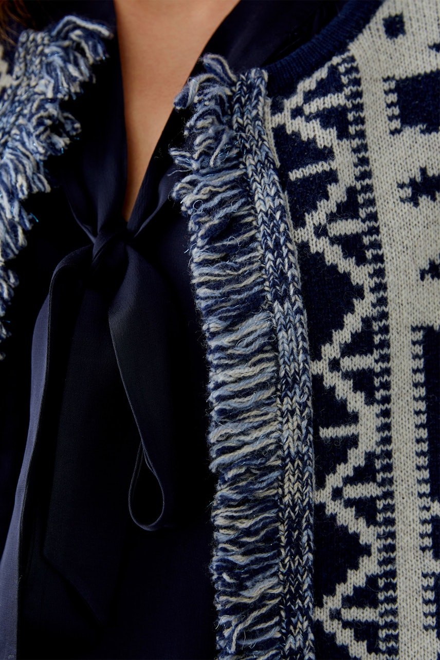Damen-Strickjacke: Frau trägt eine navyfarbene Strickjacke mit fransigen Details und grafischem Muster.