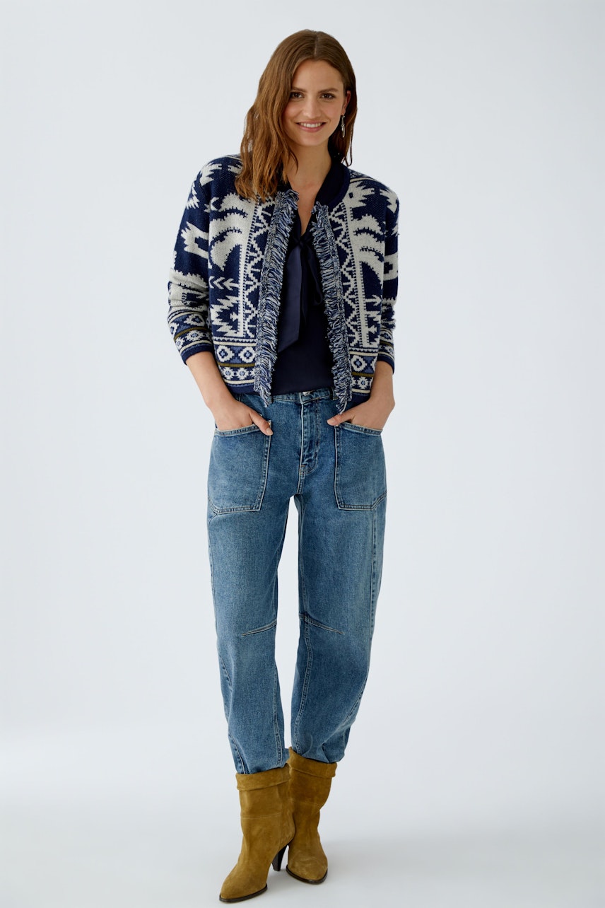 Damen-Strickjacke: Frau in blauer Strickjacke mit Muster und lässigen Jeans, strahlt Freude aus.