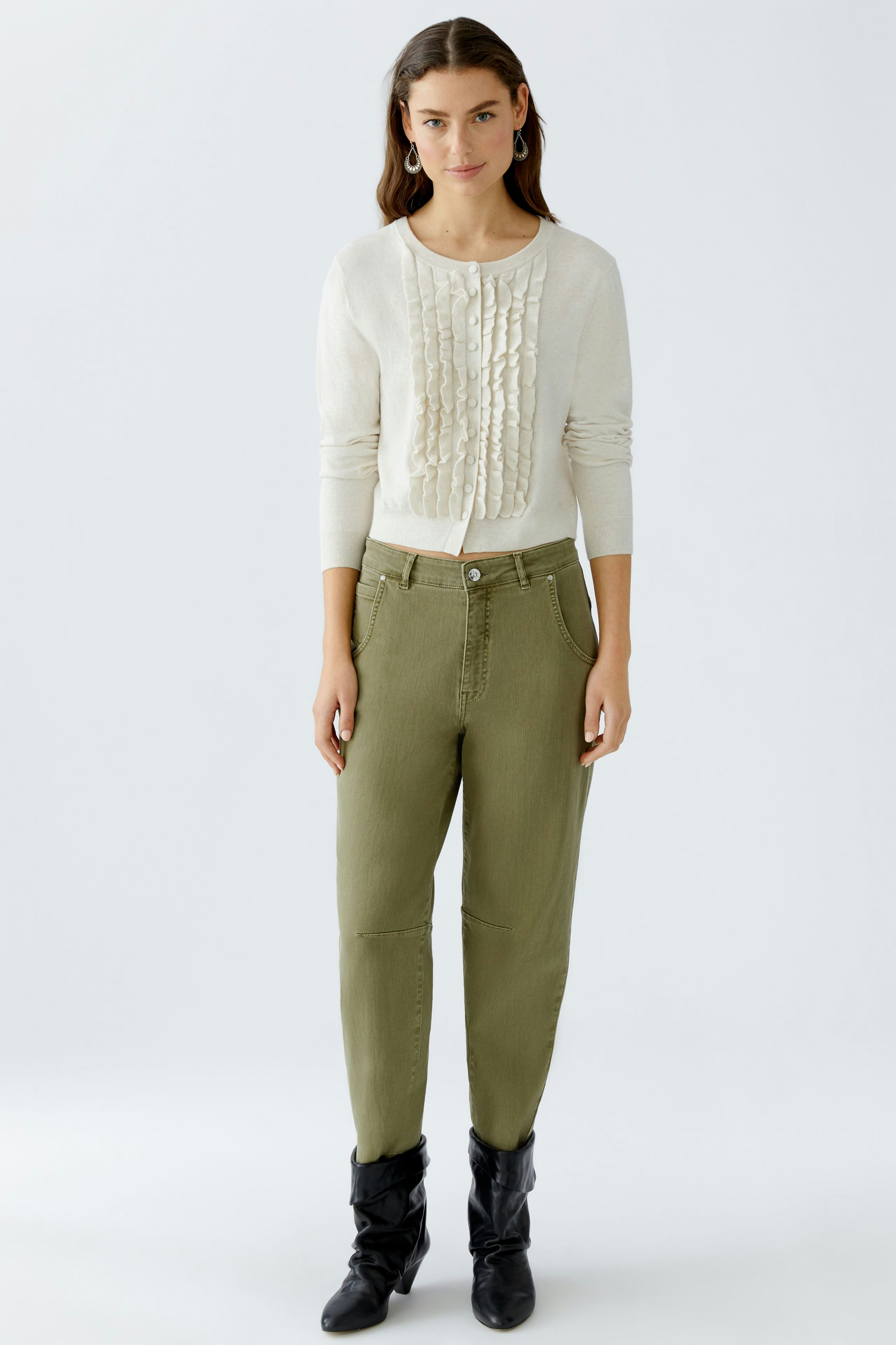 Casual women's cardigan: A woman in a cream cardigan with ruffled details and olive green pants stands confidently.