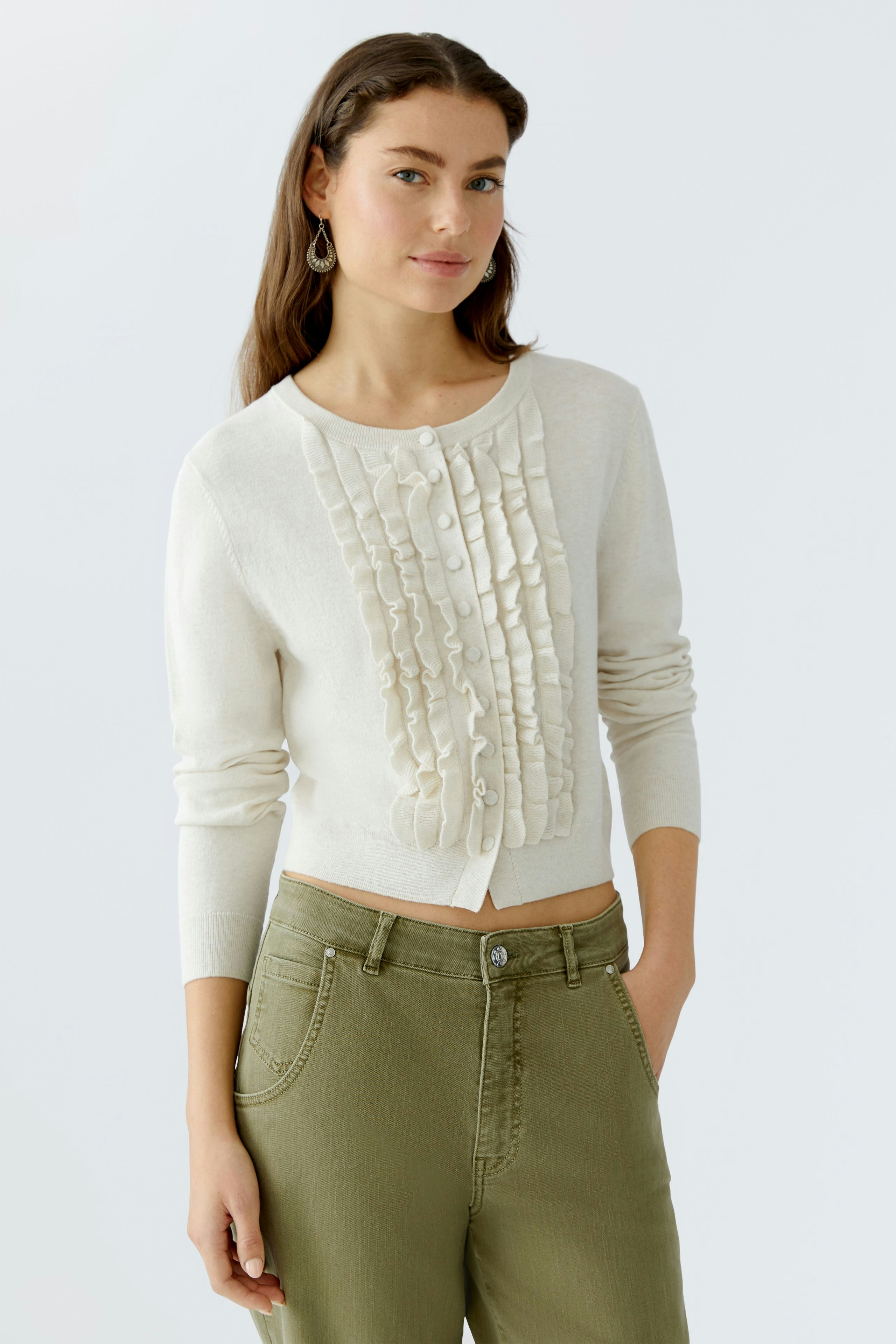 Casual women's cardigan: A woman in a cream cardigan with ruffles and buttons, paired with green pants.