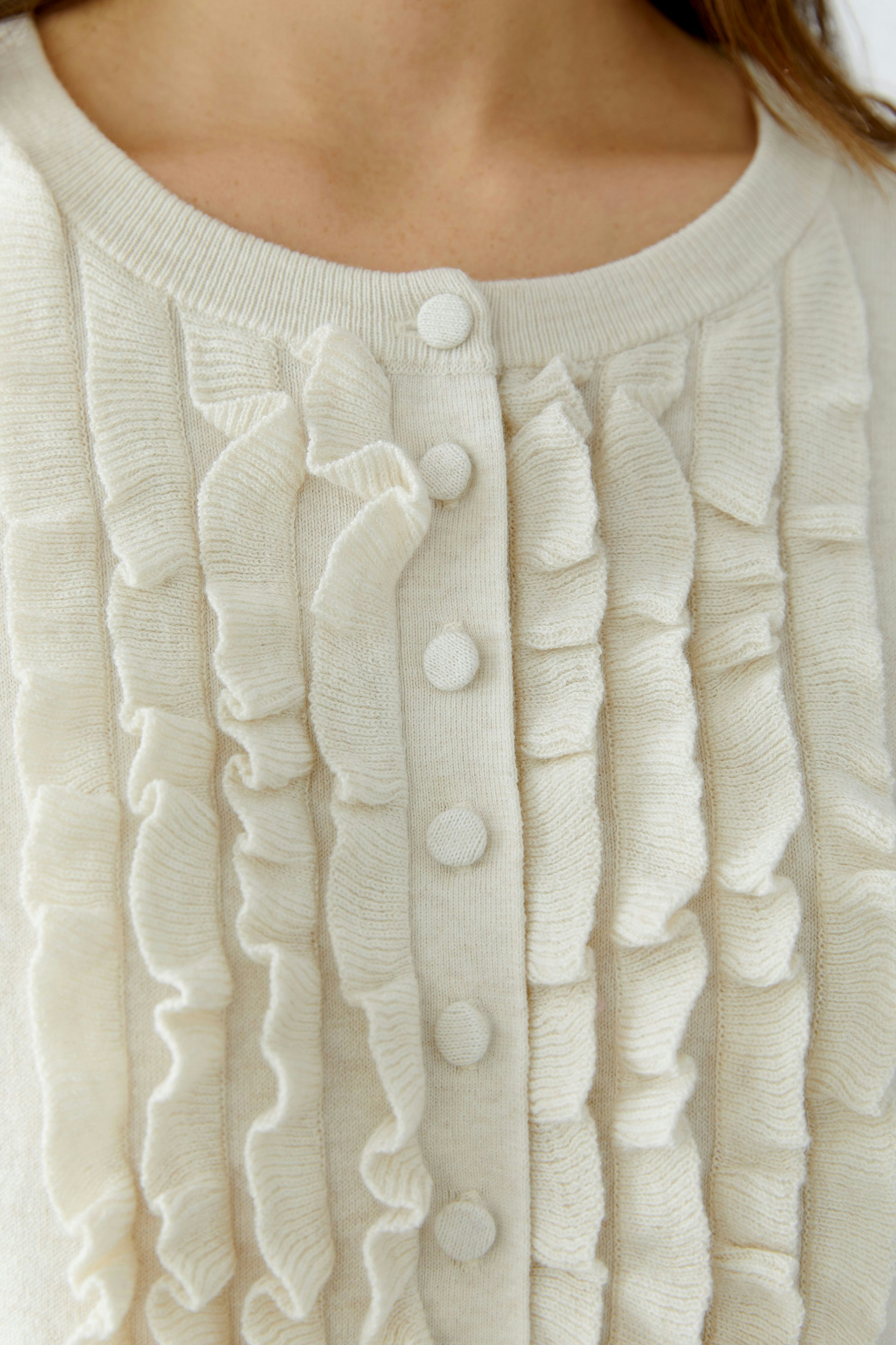 Casual women's cardigan: Close-up of a woman in a cream cardigan with ruffles and buttons.