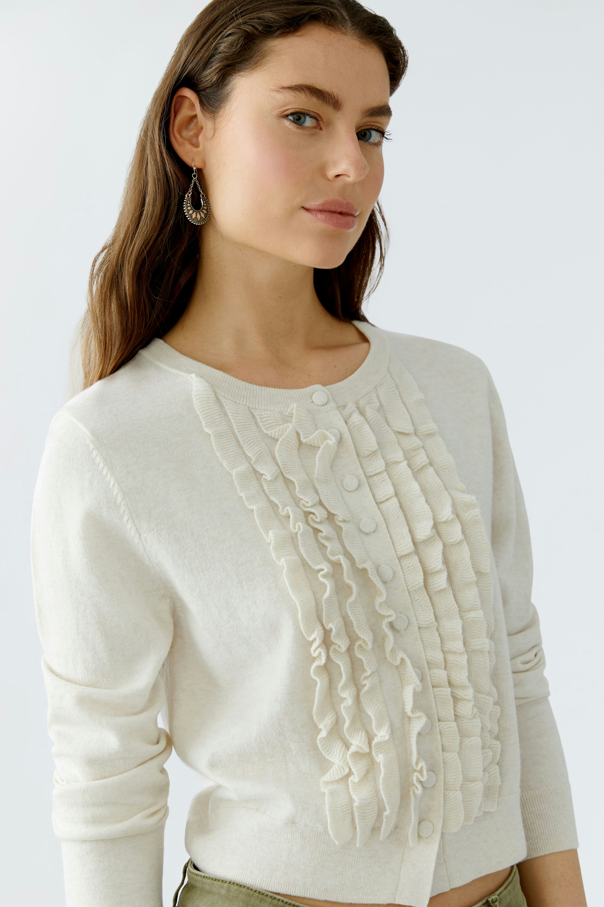 Casual women's cardigan: A woman in a cream cardigan with ruffles and buttons, looking relaxed.