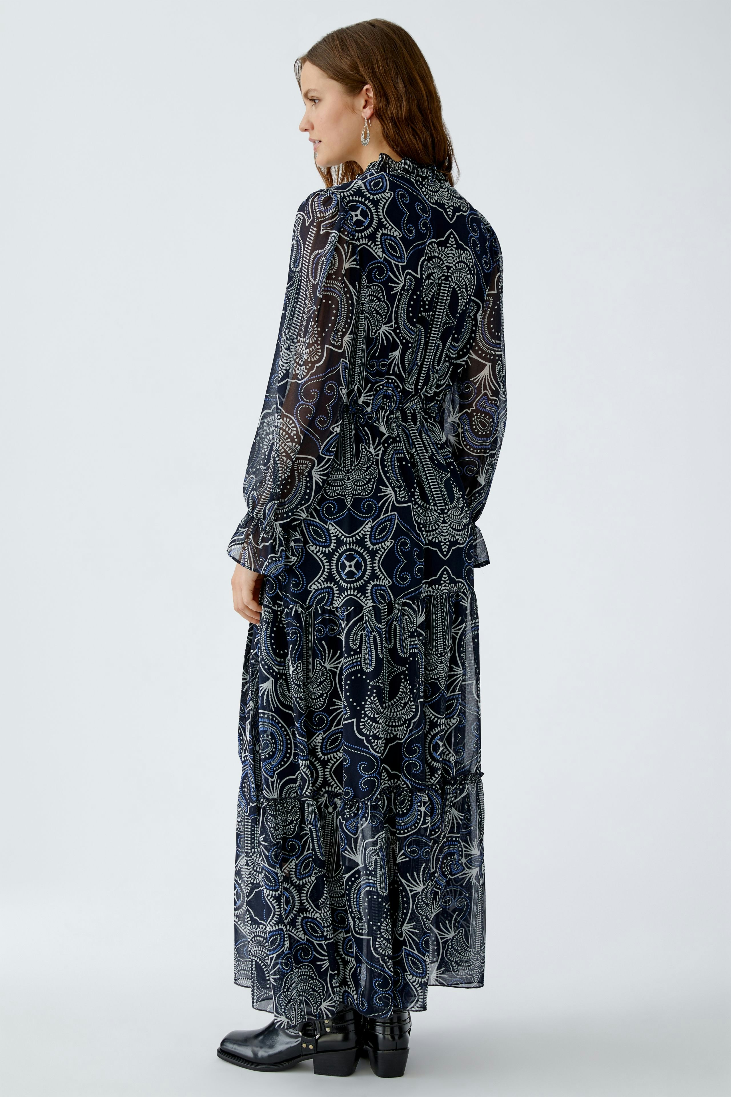Flowy maxi dress: Woman in a patterned navy dress with long sleeves and tiered design.