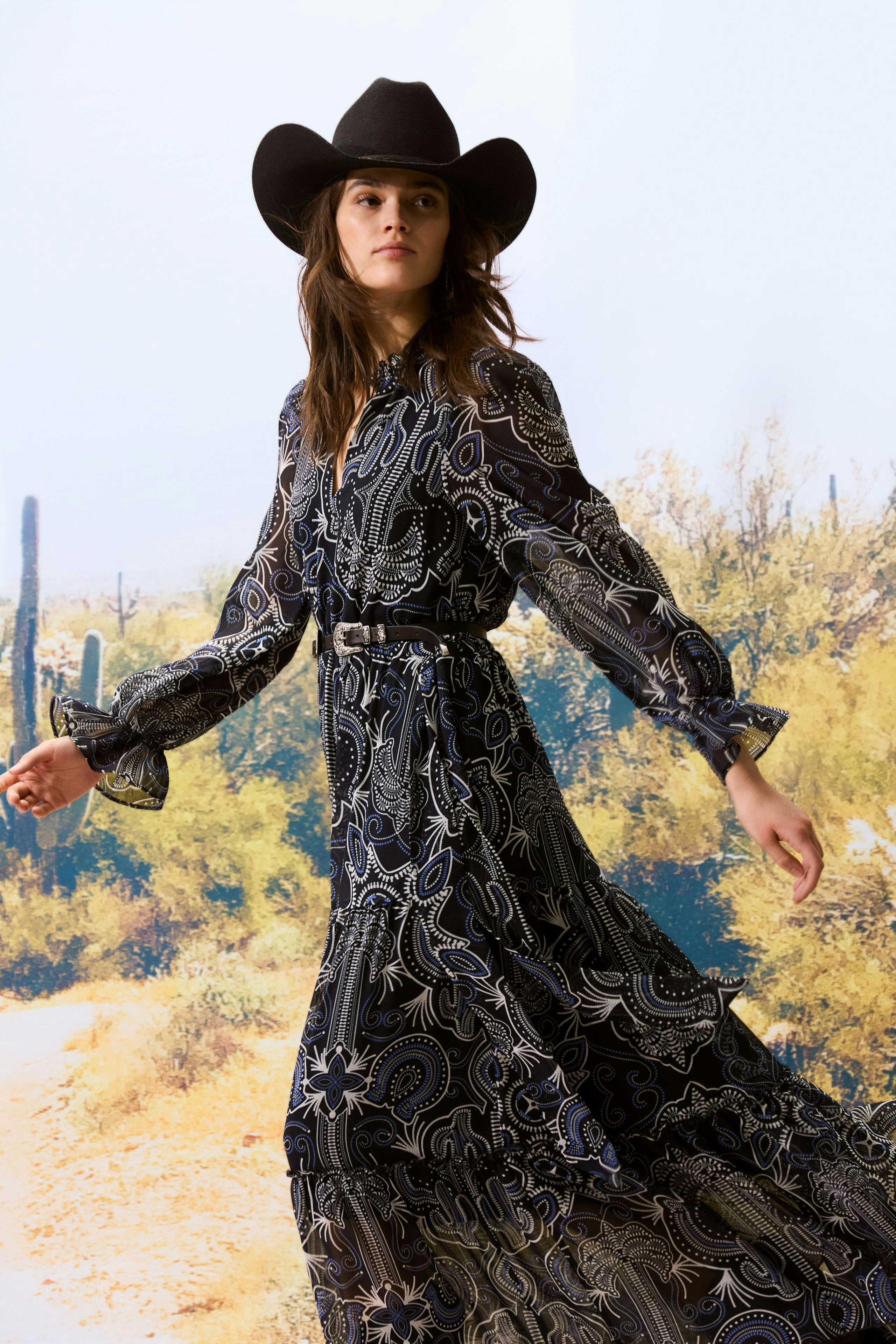 Flowy maxi dress: Woman in a patterned long dress with a belt, styled with a black cowboy hat.