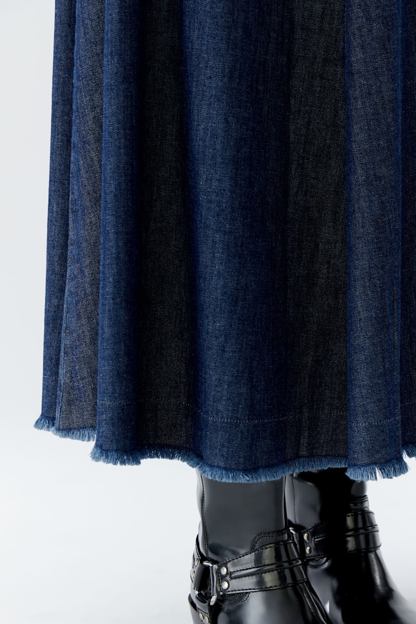 Damen-Jeansrock: Lässige Frau in einem dunkelblauen Jeansrock mit fransigem Saum und schwarzen Stiefeln.