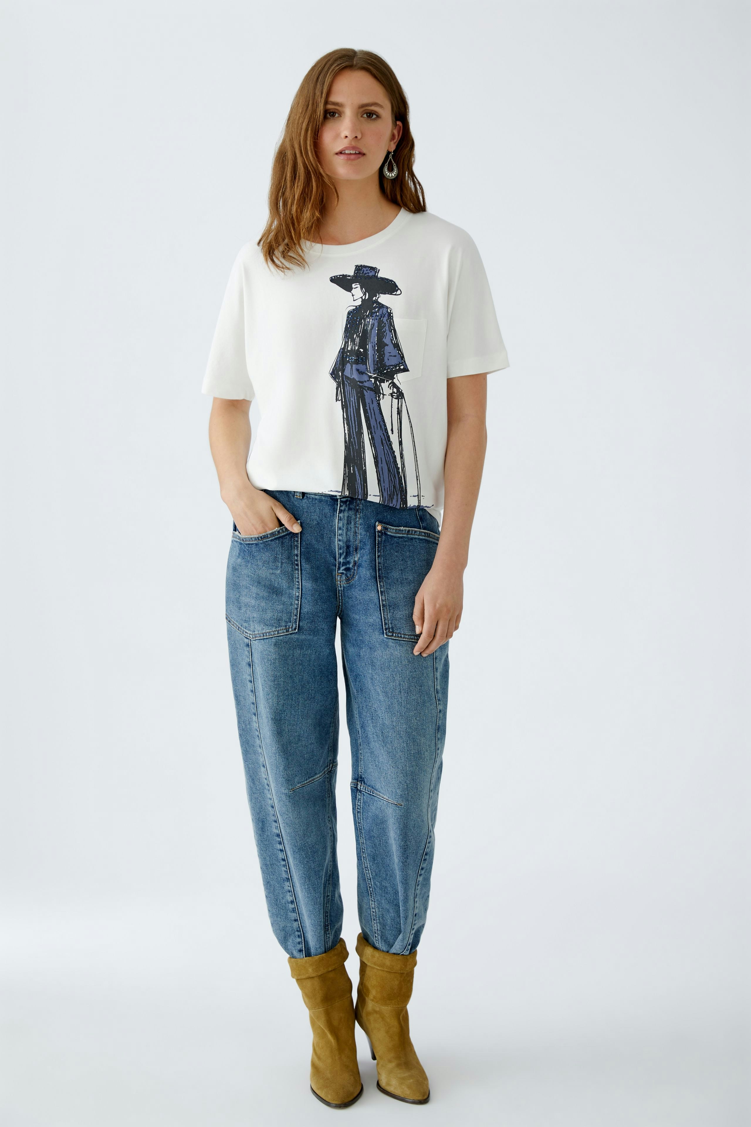 Damen-T-Shirt: Frau in weißem T-Shirt mit grafischem Druck und lässigen Jeans steht entspannt.