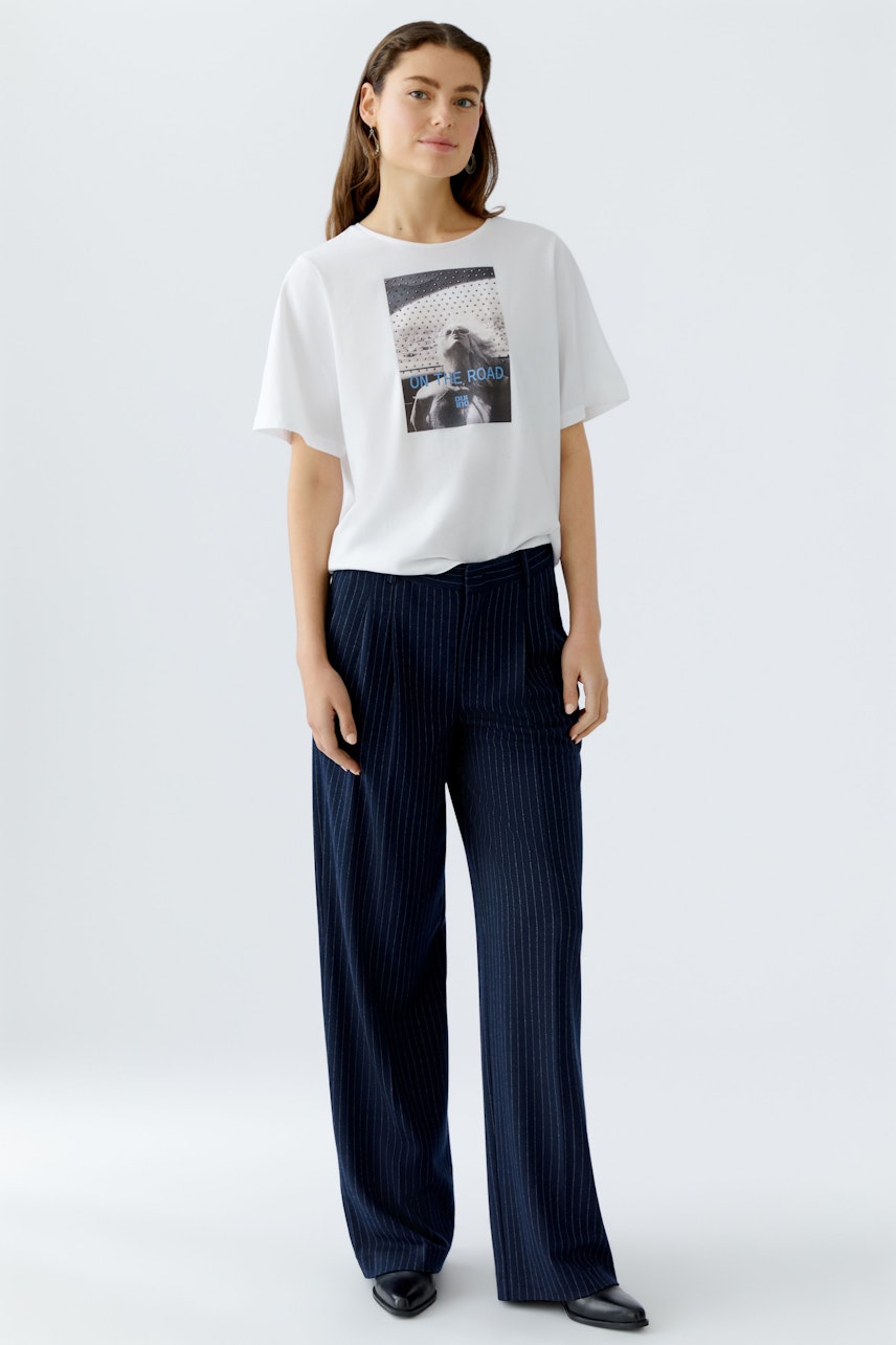 Damen-T-Shirt: Frau in weißem T-Shirt mit grafischem Print und lässigen, gestreiften Hosen.