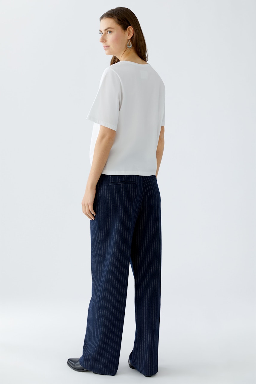 Damen-T-Shirt: Frau in weißem T-Shirt mit kurzen Ärmeln und lässigen, blauen Hosen von hinten.