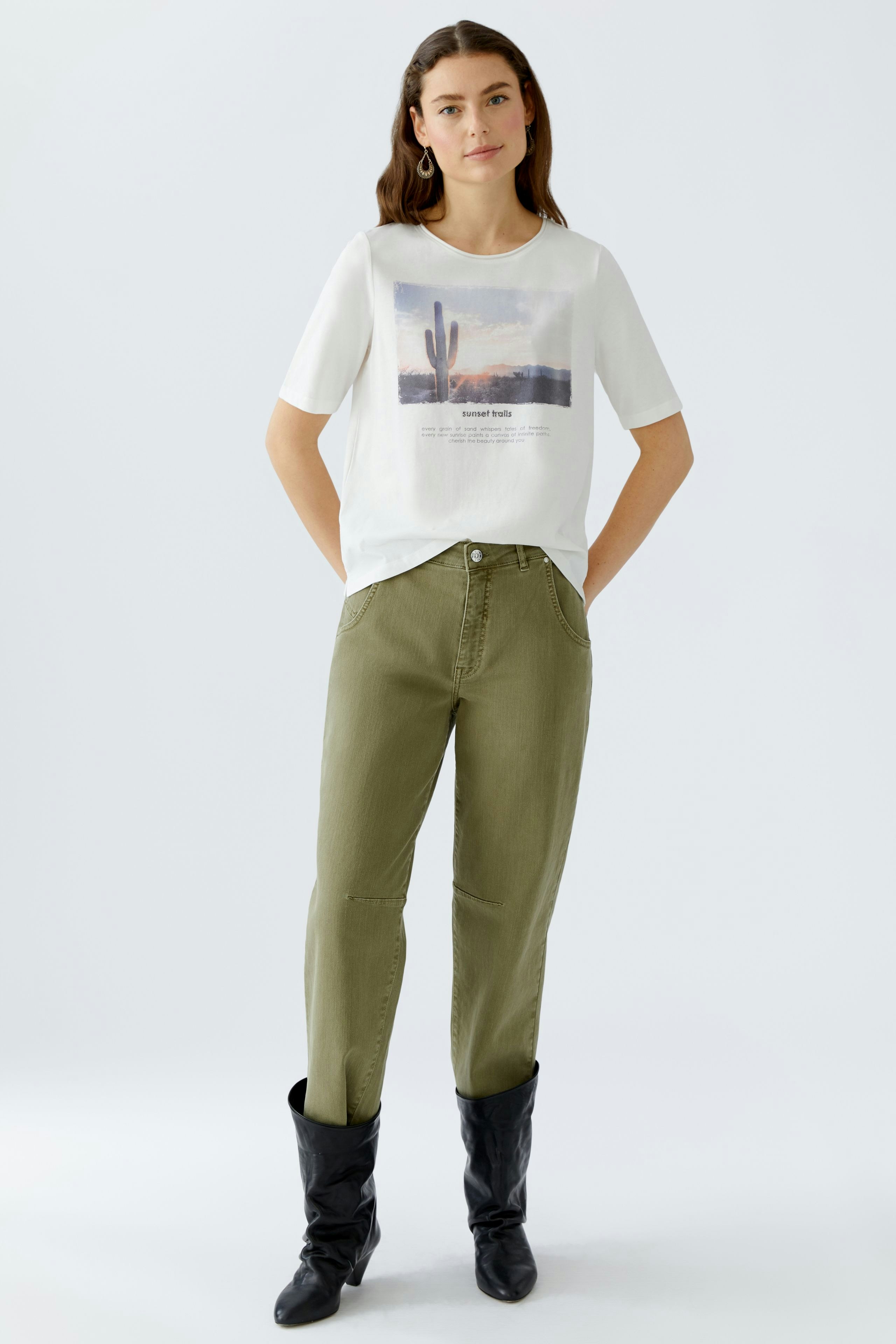 Damen-T-Shirt: Junge Frau trägt ein weißes T-Shirt mit einem bunten Wüstenmotiv und lässigen Hosen.
