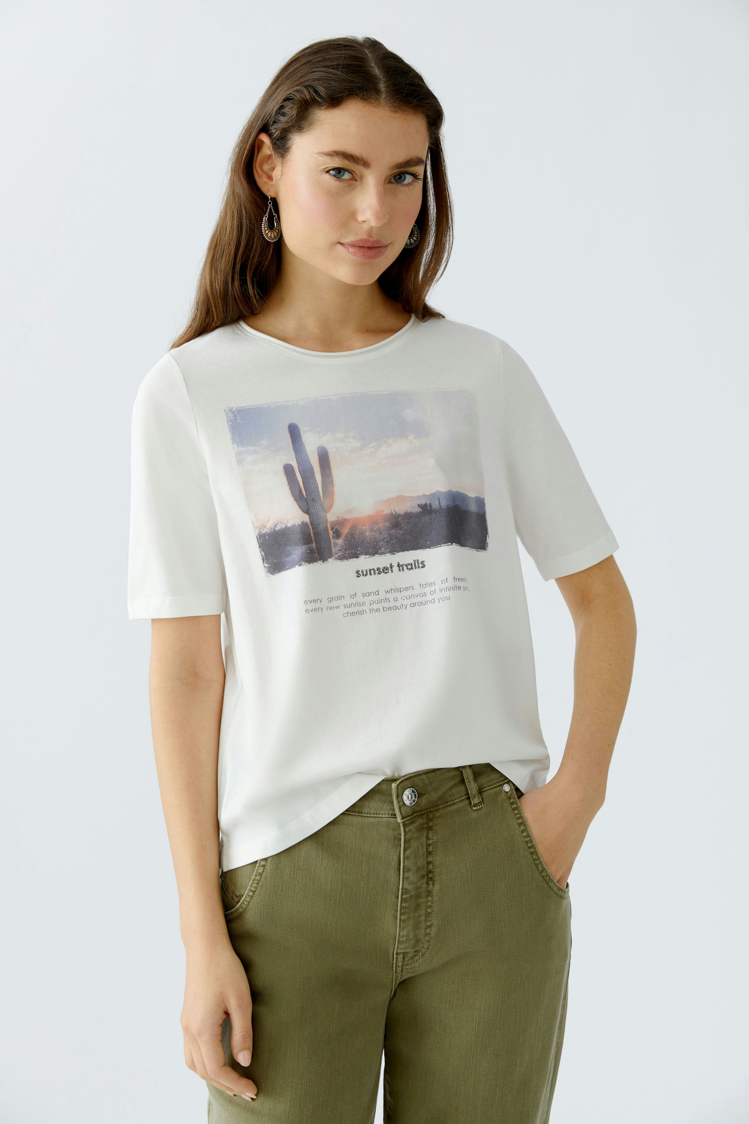 Damen-T-Shirt: Frau in weißem Shirt mit Grafik und lässigen Hosen, entspannt und modisch.