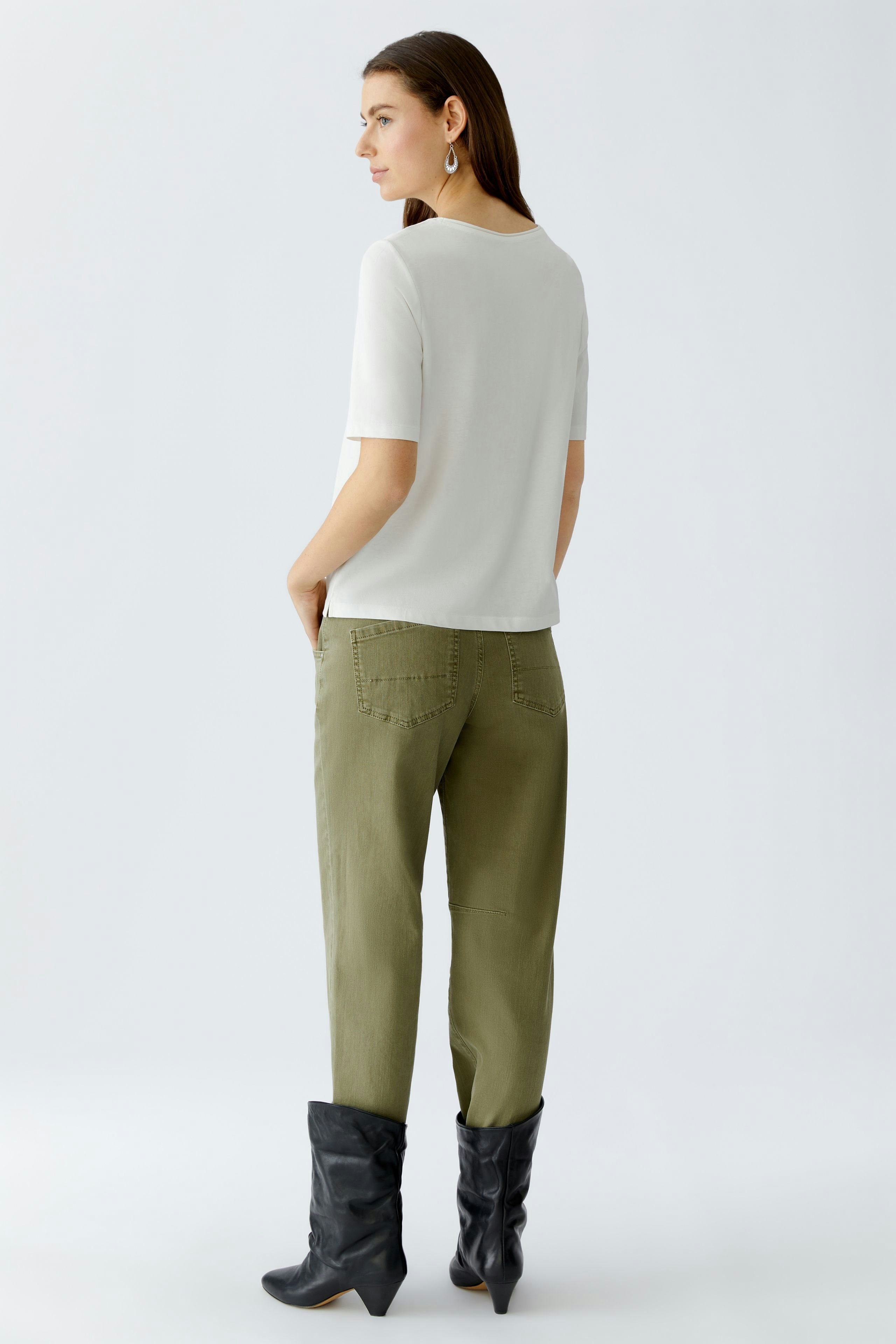 Damen-T-Shirt: Frau in weißem T-Shirt mit kurzen Ärmeln und lässigen Hosen, entspannt stehend.