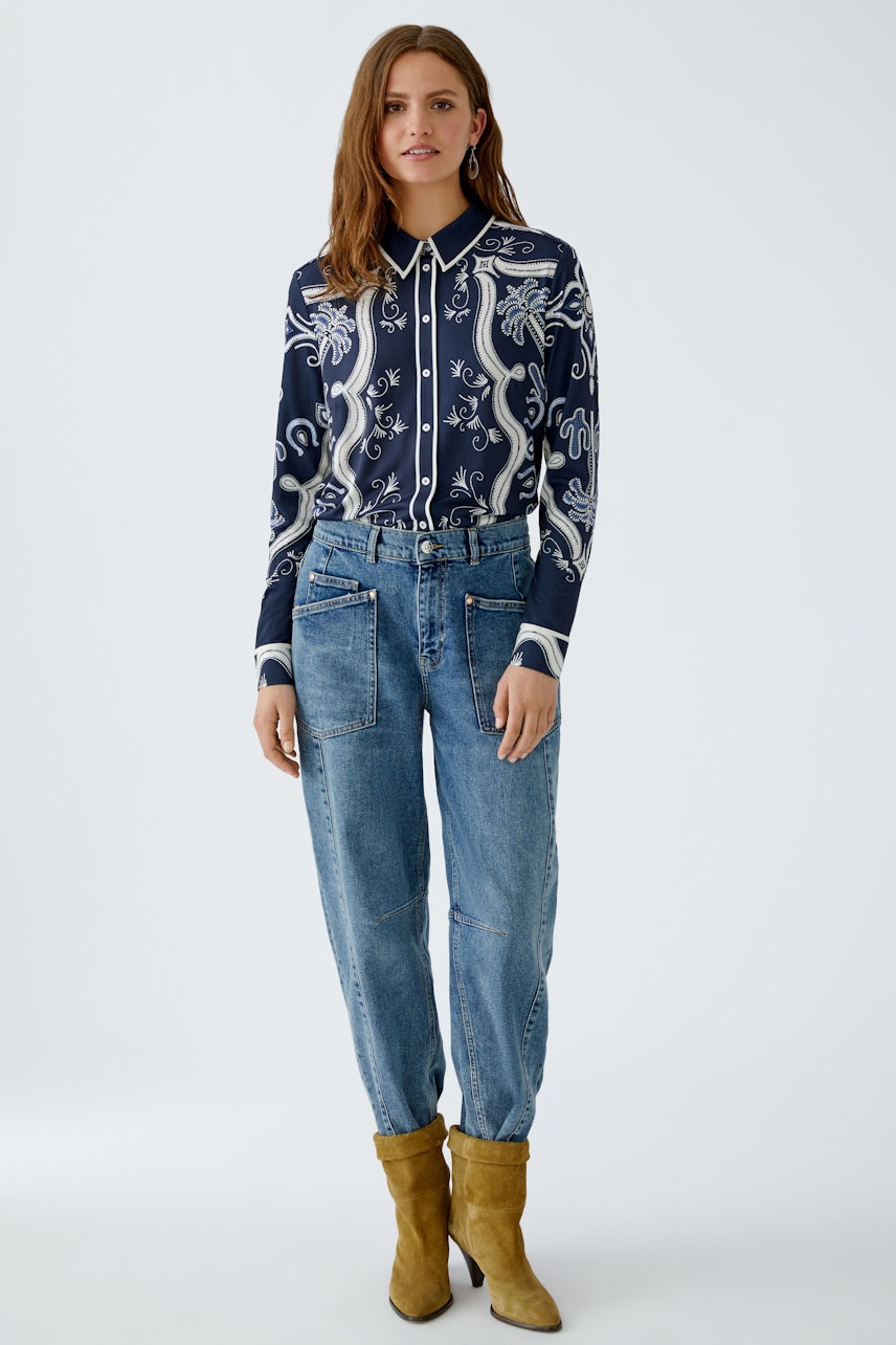 Damen-Bluse mit floralem Muster: Frau trägt eine navyfarbene Bluse mit weißen Details und lässigen Jeans.
