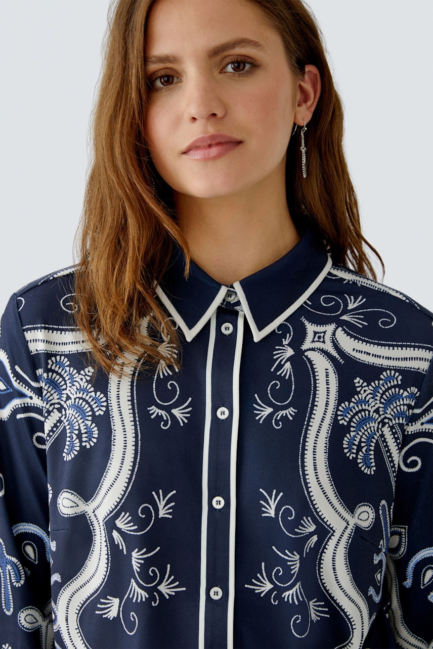 Damen-Bluse: Frau trägt eine navyfarbene Bluse mit floralem Muster und klassischem Kragen.