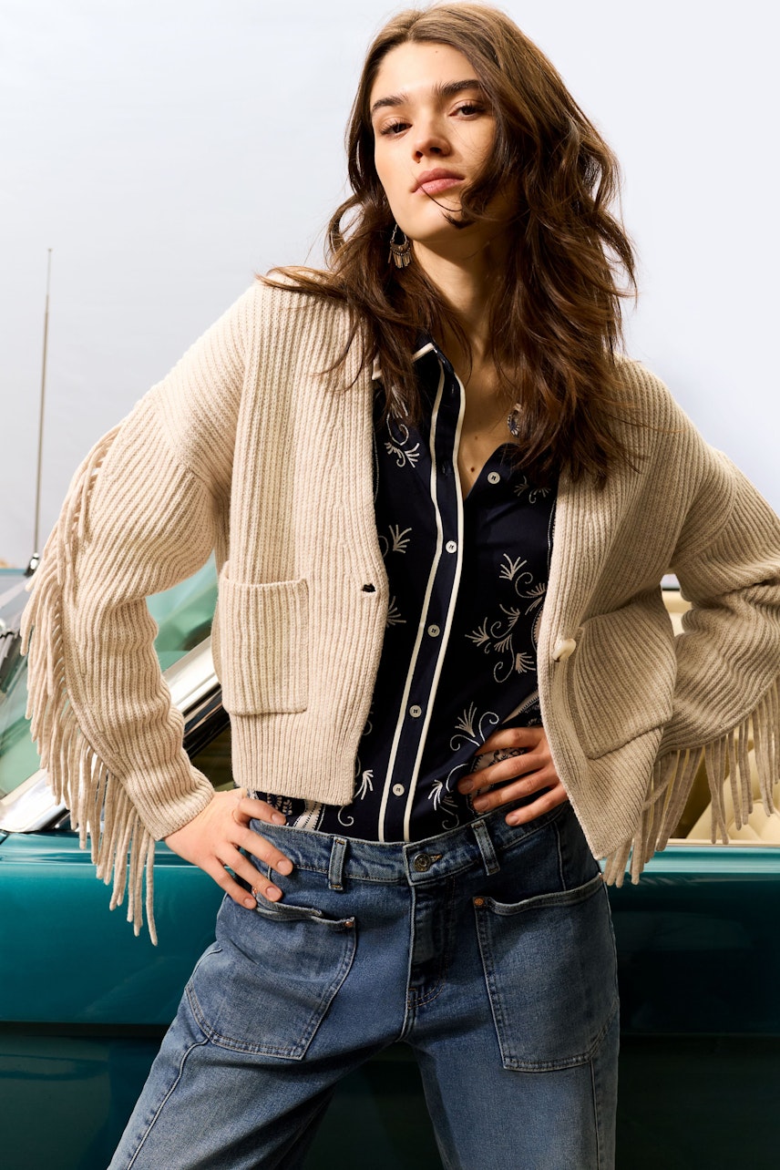Damen-Bluse: Junge Frau in einer blauen Bluse mit floralem Muster und lässiger Fransenjacke.