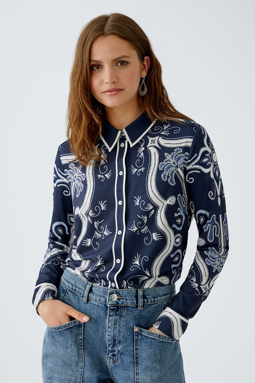 Damen-Bluse: Frau in navyfarbener Bluse mit floralem Muster und Knopfleiste, kombiniert mit Jeans.