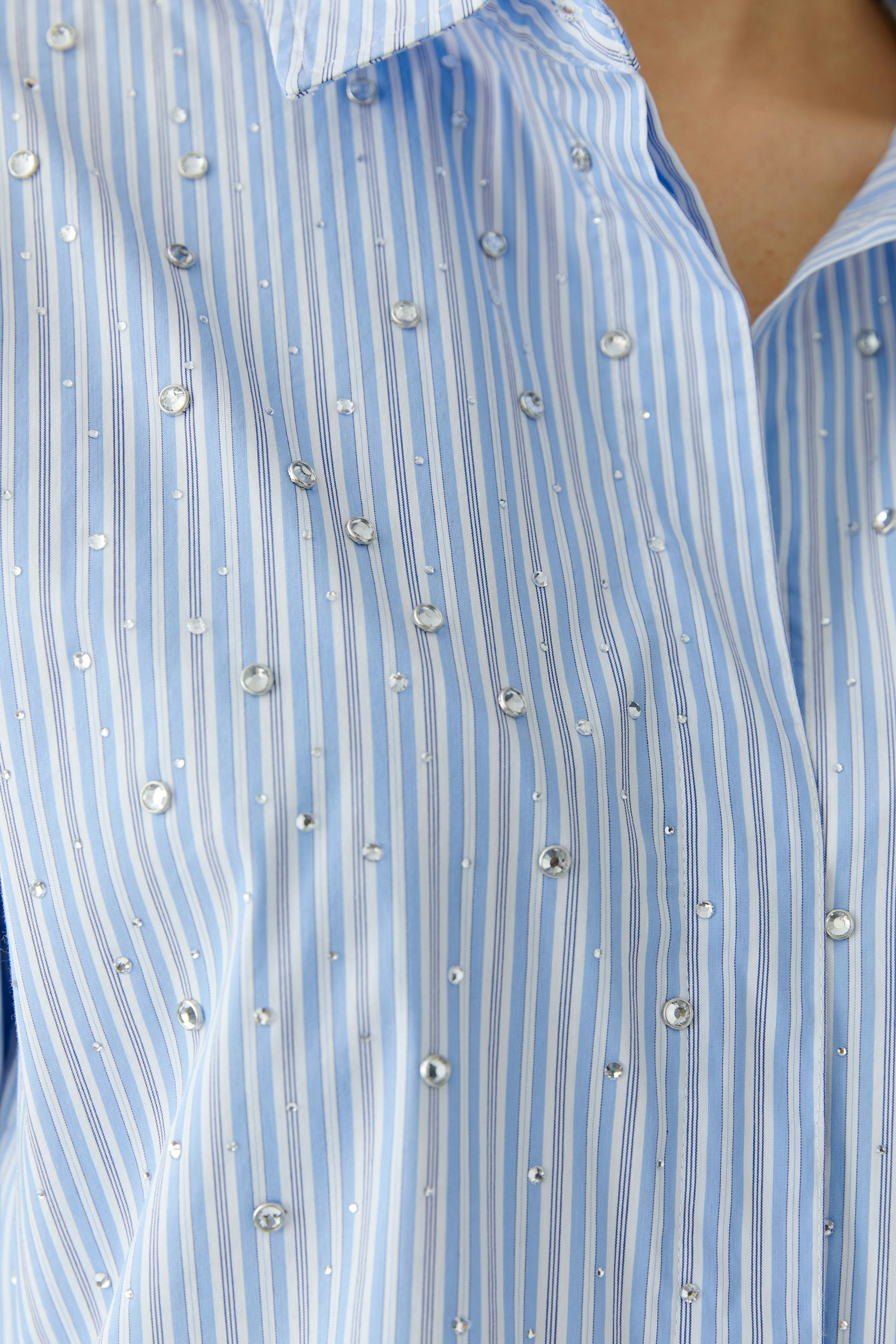 Casual women's blouse: Close-up of a woman in a light blue striped blouse with decorative gems.