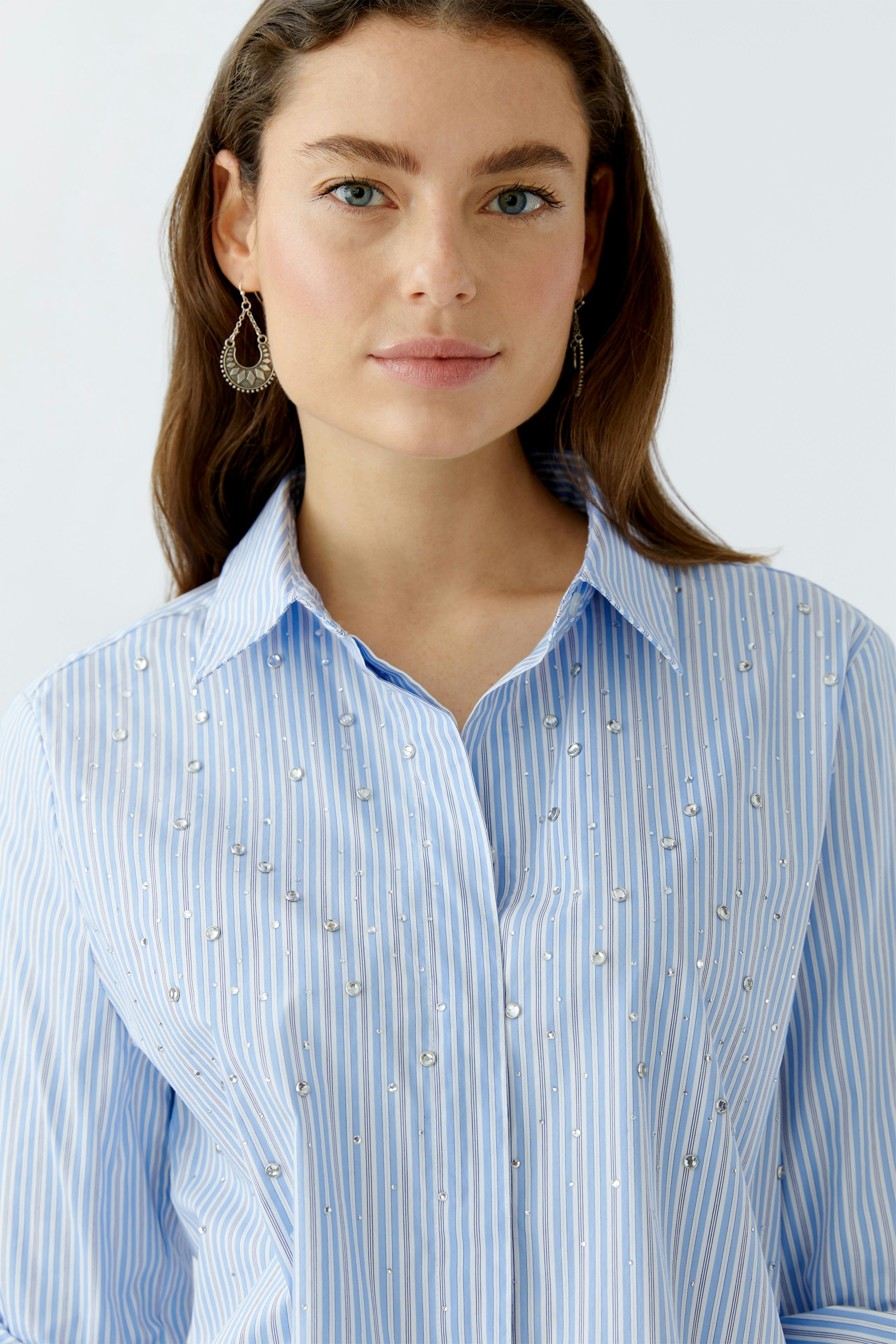 Casual women's blouse: Woman in a light blue striped blouse with decorative embellishments.
