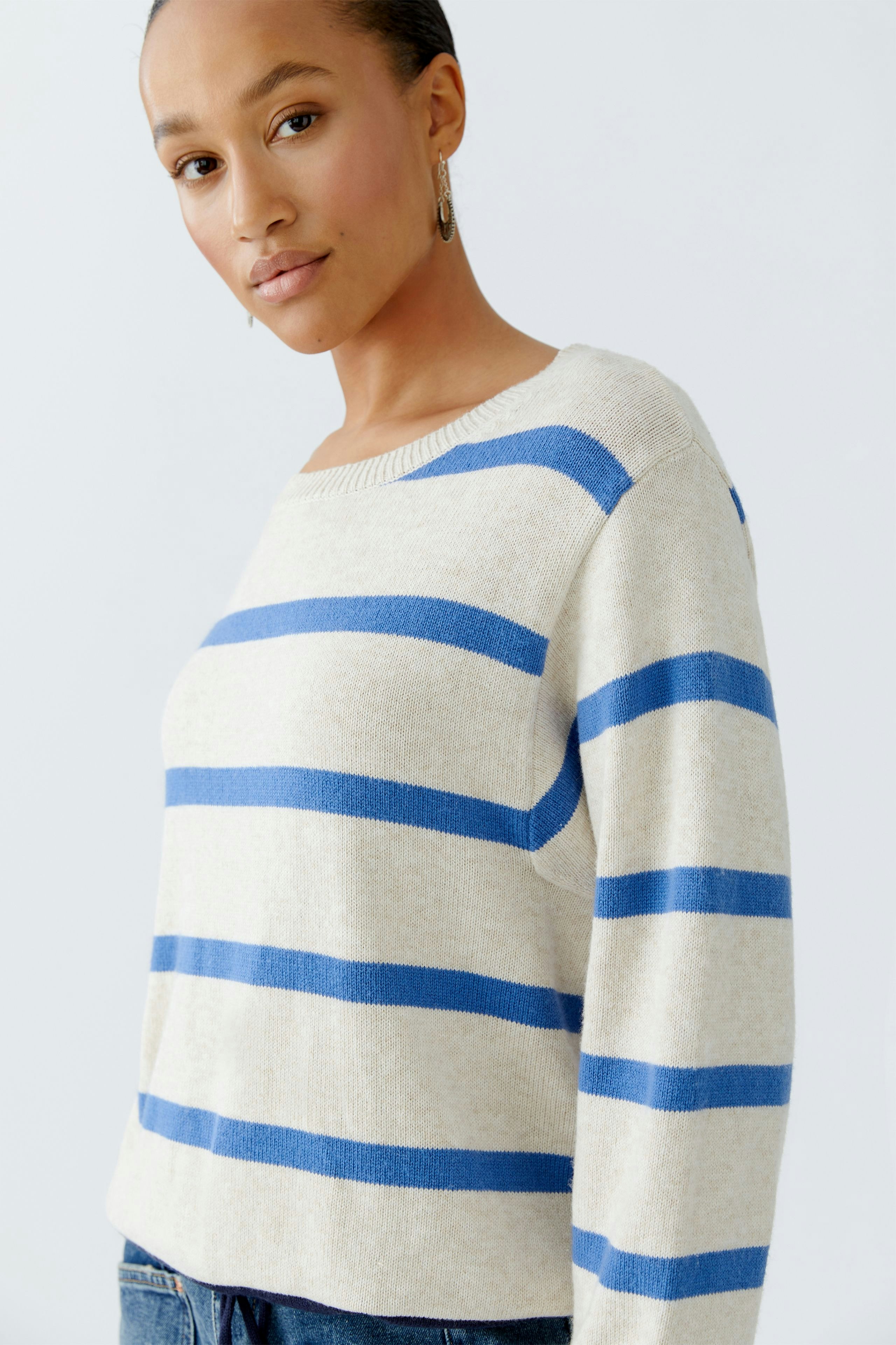 Casual women's pullover: A woman in a beige pullover with blue stripes, looking confidently at the camera.