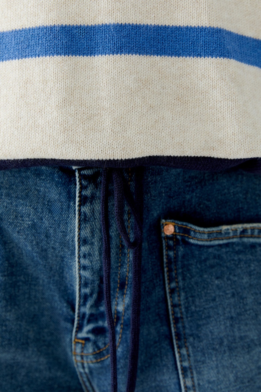 Bequemer Damen-Pullover in Creme mit blauen Streifen, lässig über Jeans getragen.
