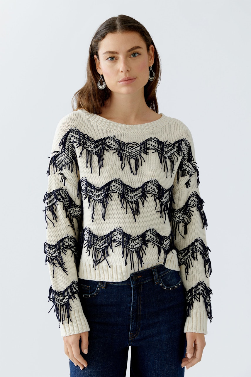 Casual women's pullover: Young woman in a cream pullover with navy fringes and jeans.