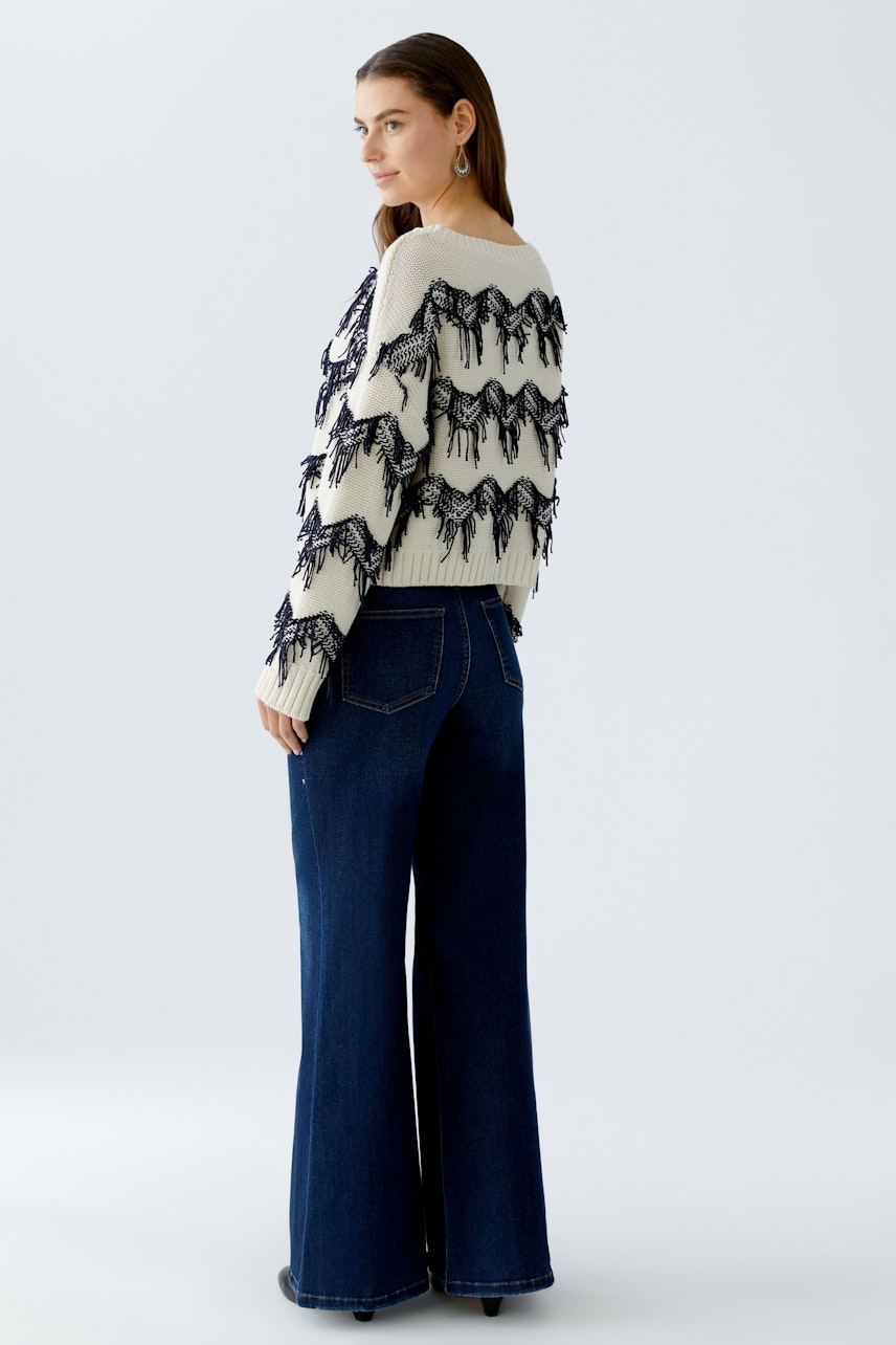 Casual women's pullover: A woman in a cream pullover with black fringes and wide-leg jeans.