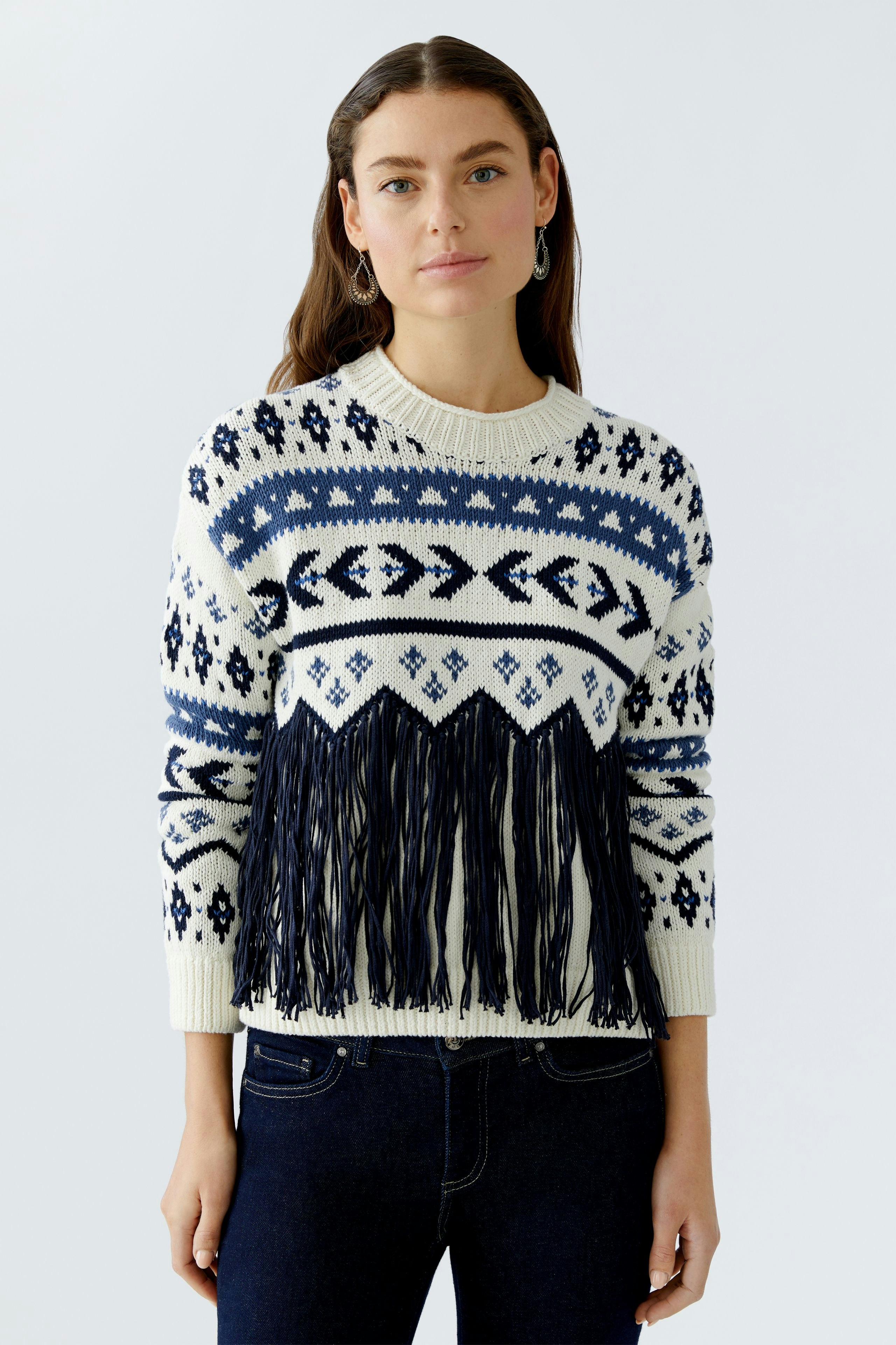 Modern women's pullover: Young woman in a patterned pullover with fringes, paired with dark jeans.
