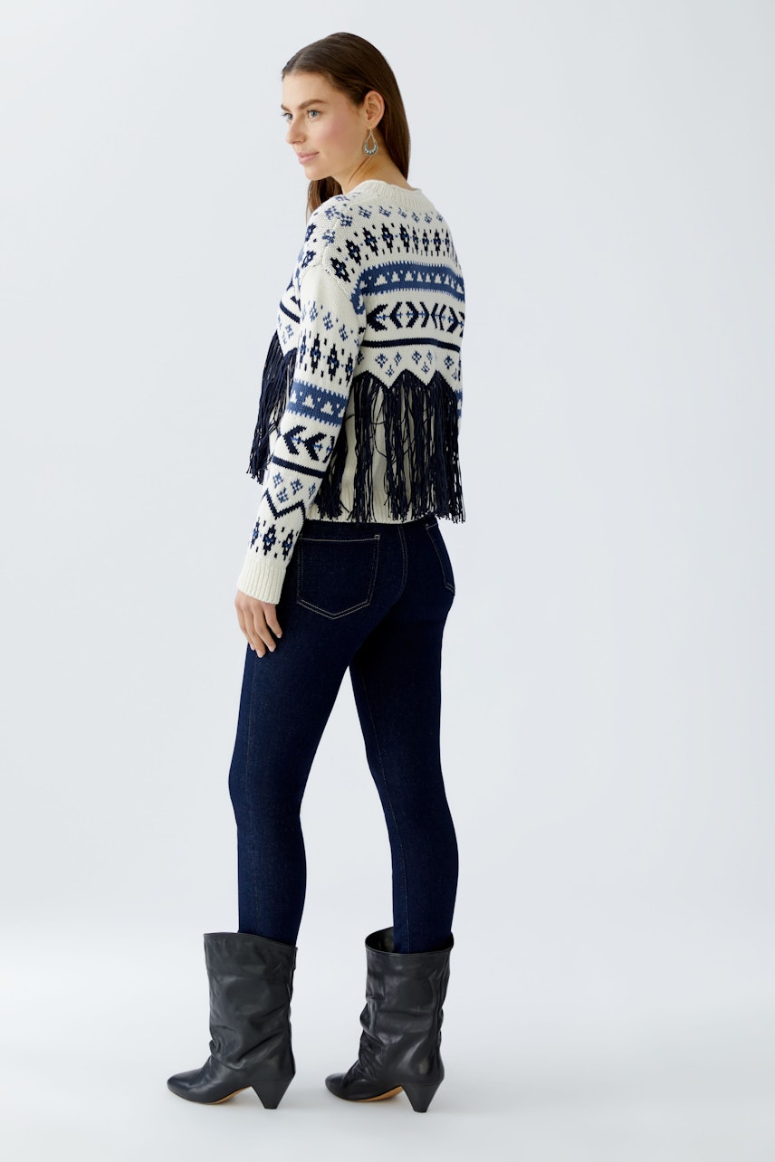 Casual women's pullover: Woman in a fringed knit pullover with a geometric pattern and dark jeans.